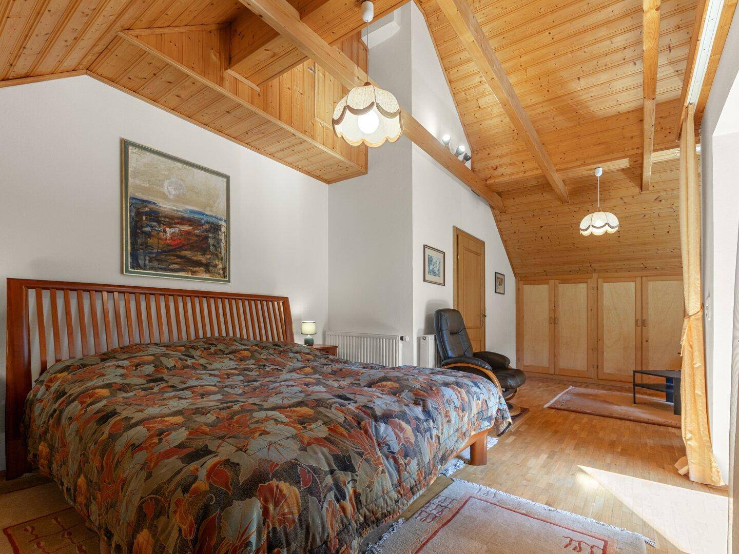 Helles Schlafzimmer mit Holzbalkendecke, großem Bett und Blick in die Natur.