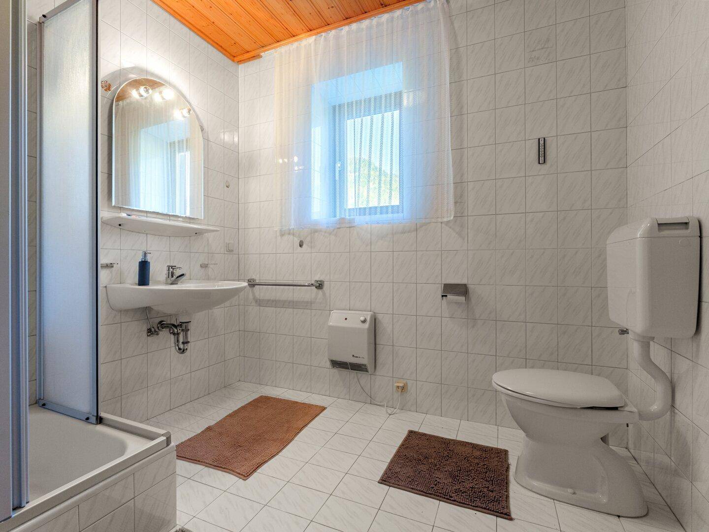 Helles Badezimmer mit weißen Fliesen, Fenster und einfacher Ausstattung.