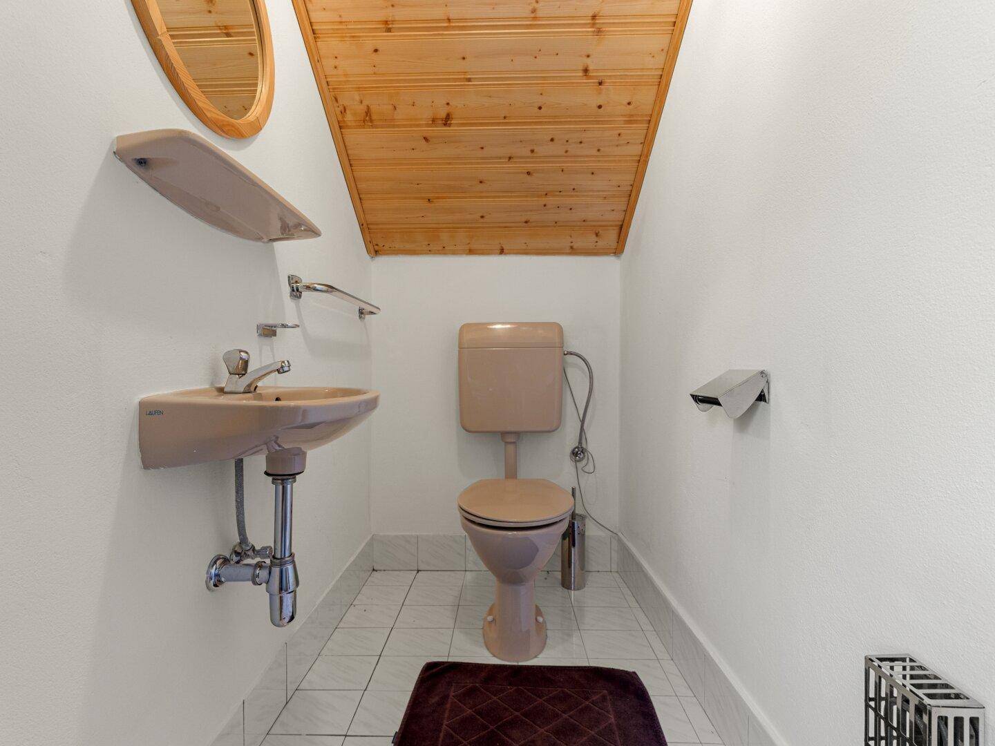 Kleines Gäste-WC mit beiger Toilette, Waschbecken und Holzdecke.