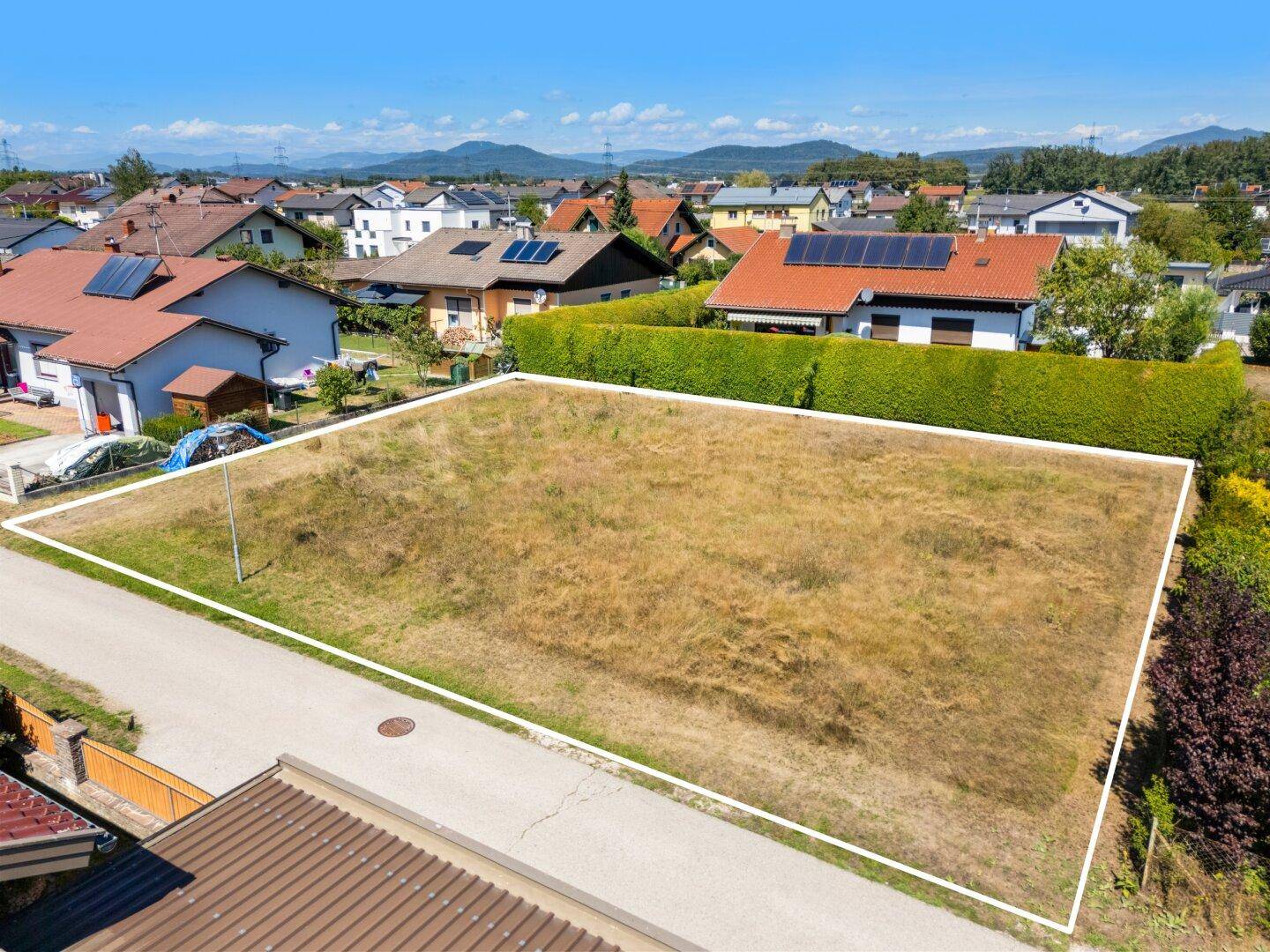 Drohnenaufnahme des Baugrundstücks mit umliegenden Häusern und Blick auf die Landschaft.
