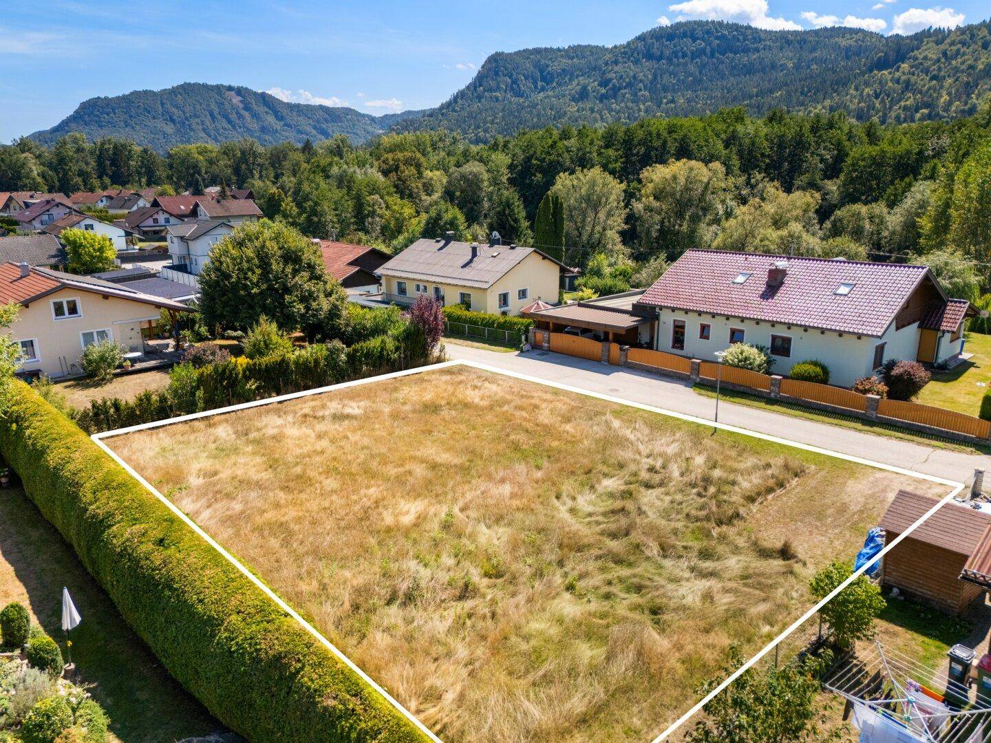 Weitläufiges Baugrundstück mit Hecke und Blick auf die bewaldeten Berge in der Ferne.