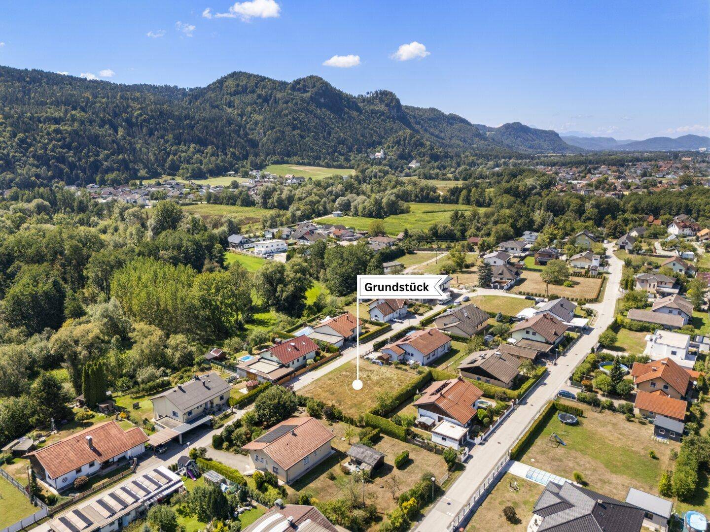 Panoramische Luftaufnahme des Baugrundstücks, umgeben von Häusern und der natürlichen Berglandschaft.