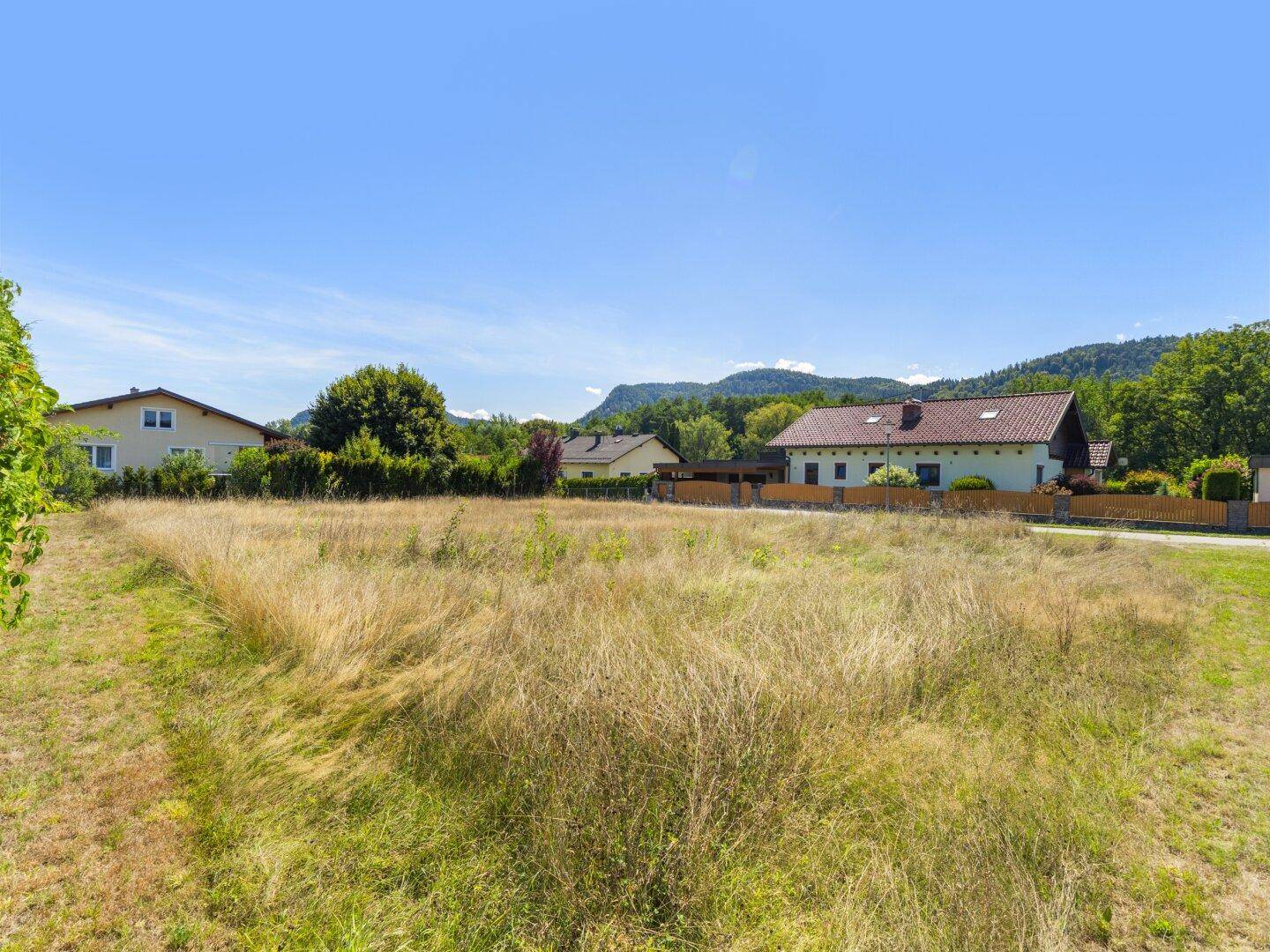 Weitläufiges Baugrundstück mit Blick auf die umliegenden Häuser und die bewaldeten Berge.