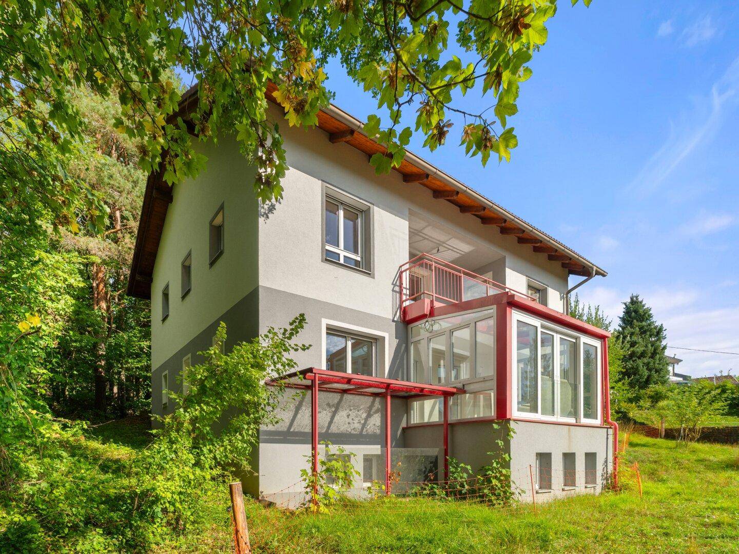 Seitenansicht des Hauses mit Wintergarten und Balkon, umgeben von üppiger Vegetation und Bäumen.