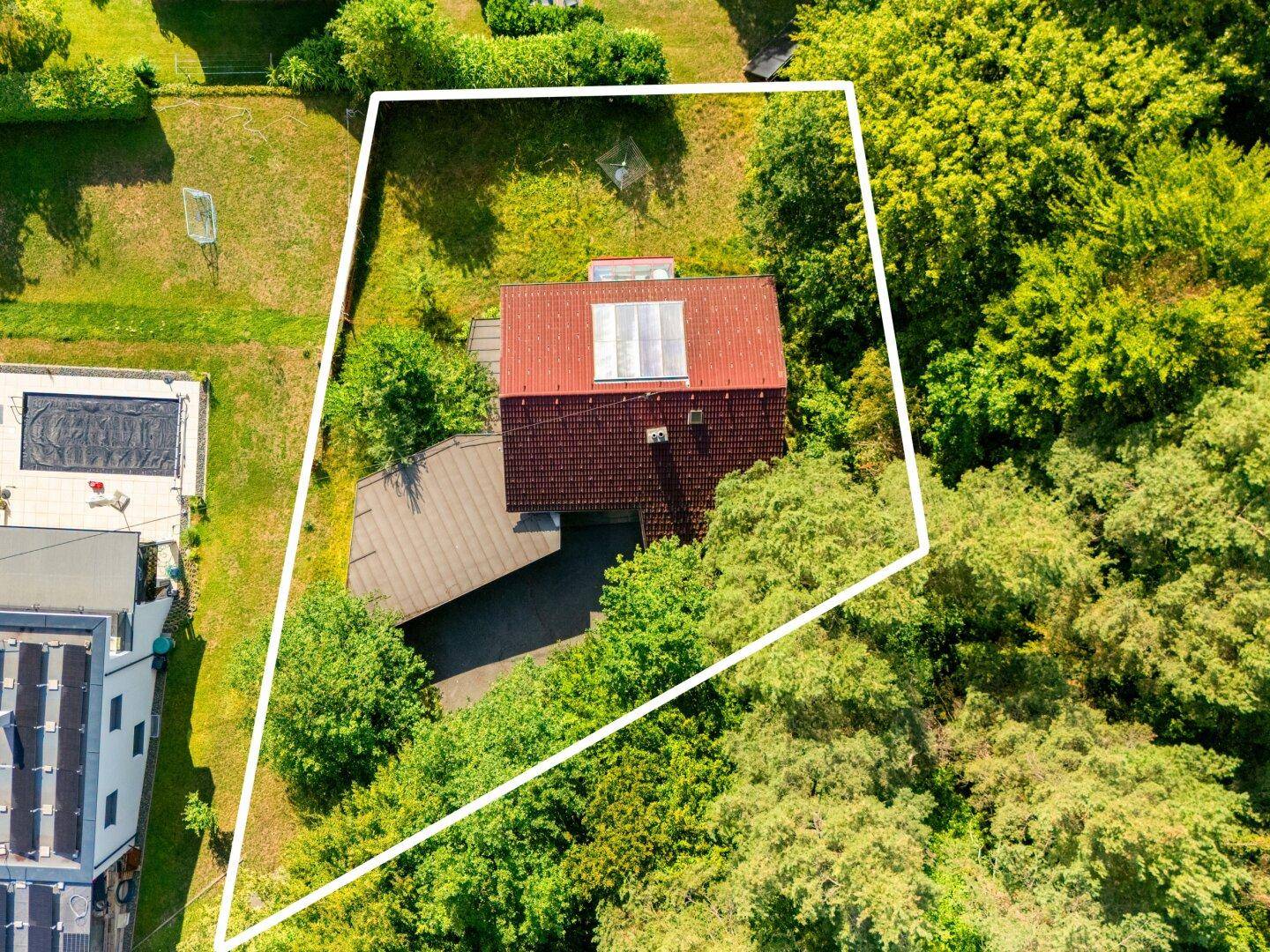 Luftaufnahme des Grundstücks mit Einfamilienhaus, umgeben von Wald und Grünflächen, mit Grundstücksgrenze.