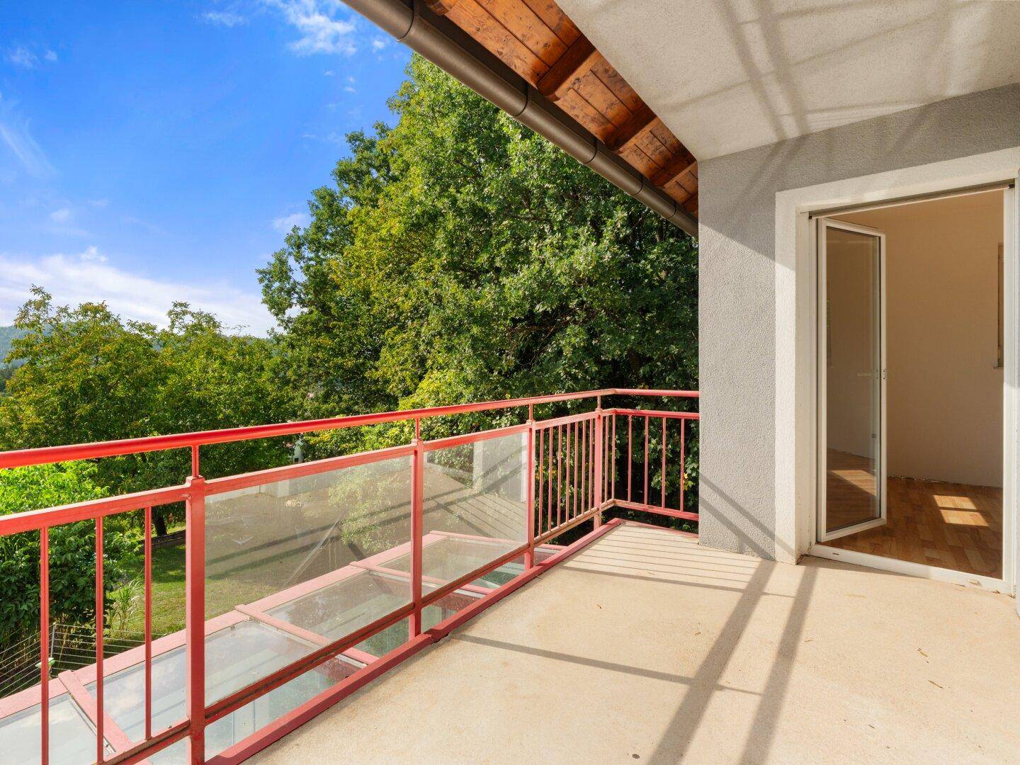 Geräumiger Balkon mit rotem Geländer und weitem Blick ins Grüne und auf die Berge.