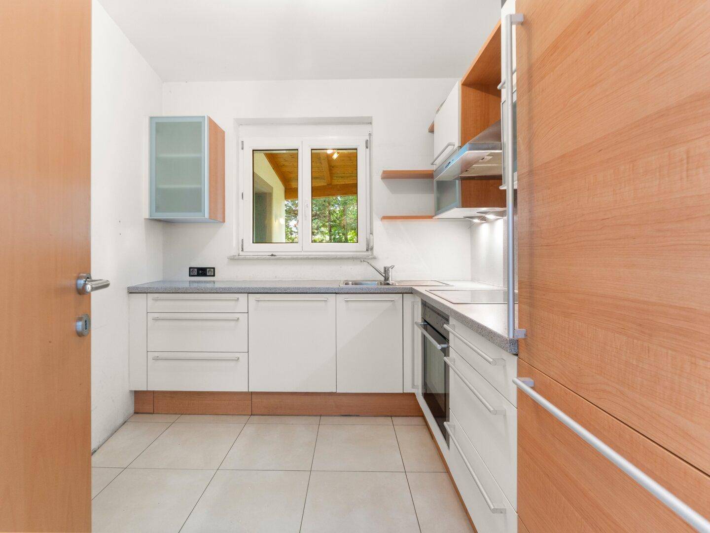 Funktionale Küche mit weißen Schränken, integriertem Backofen und Fenster mit Blick ins Grüne.
