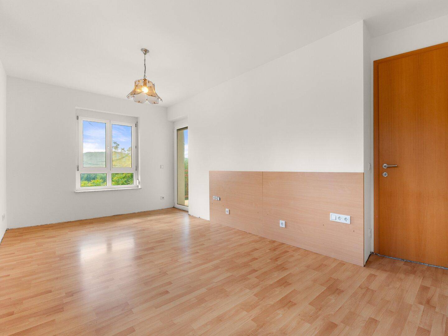 Helles Zimmer mit Laminatboden und großem Fenster, bietet viel natürliches Licht und Ausblick.