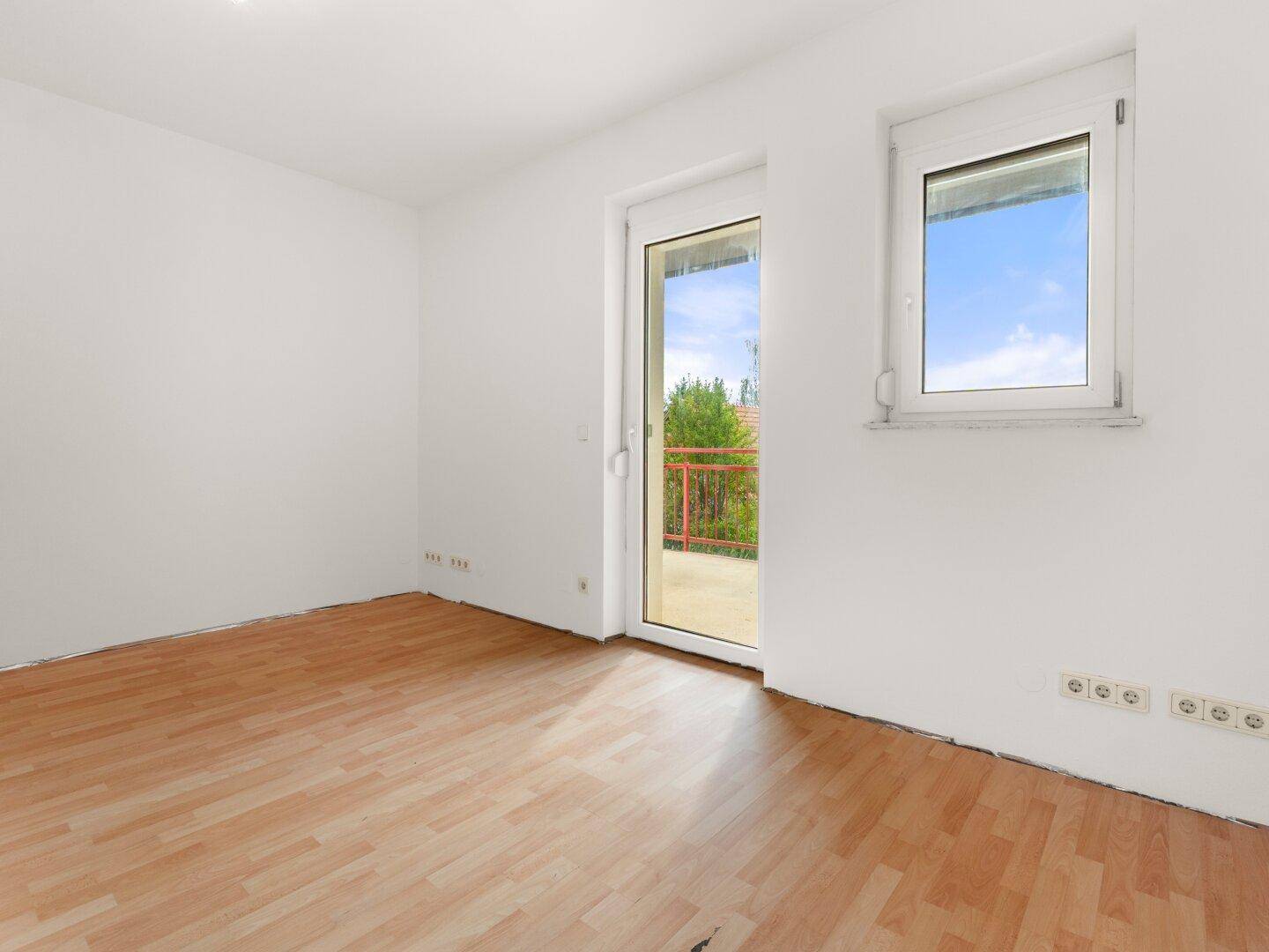 Geräumiges Zimmer mit Laminatboden und Zugang zu einem Balkon, hell und freundlich gestaltet.
