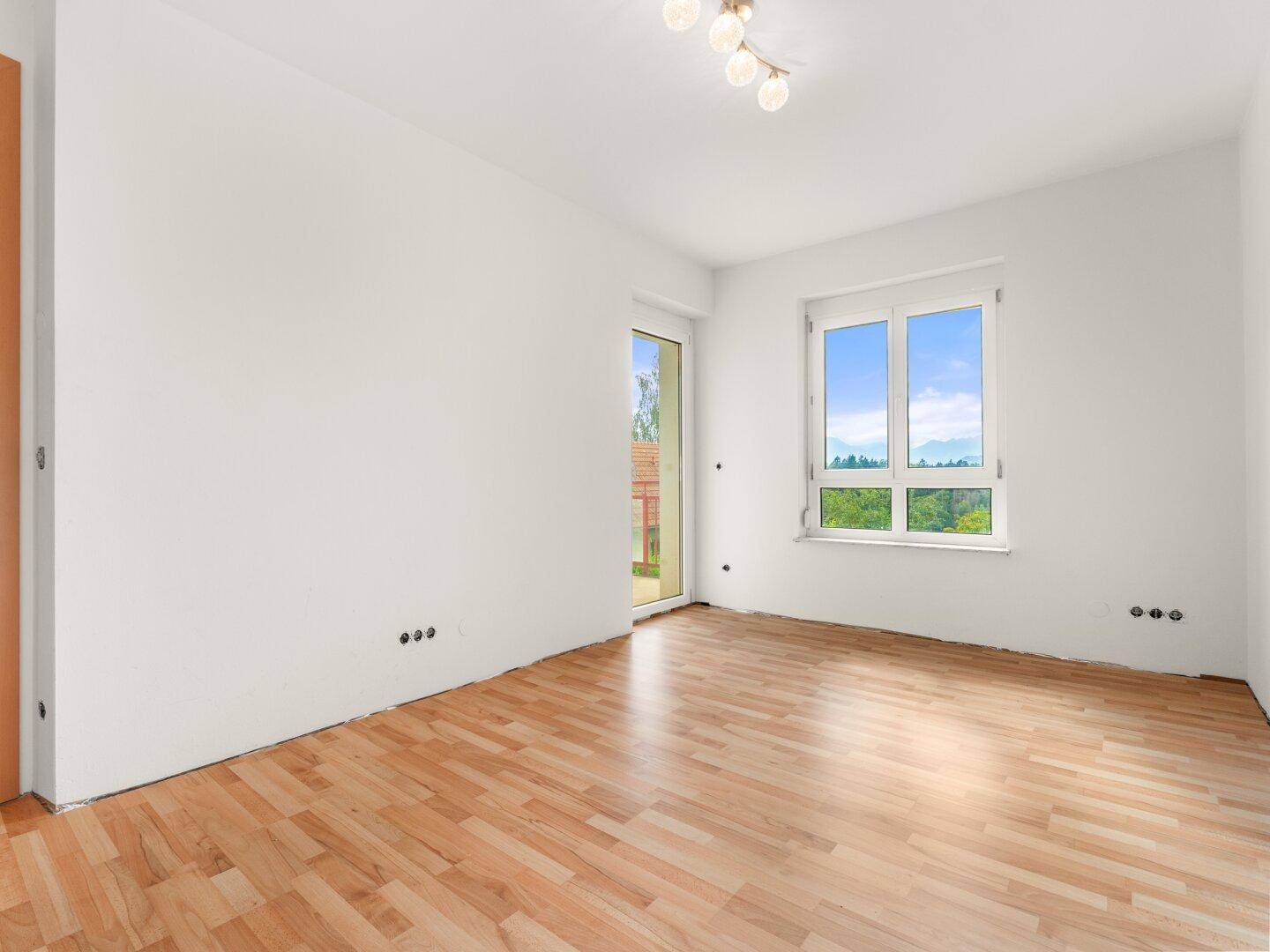 Helles Zimmer mit Laminatboden und großem Fenster, bietet einen weiten Blick ins Grüne.