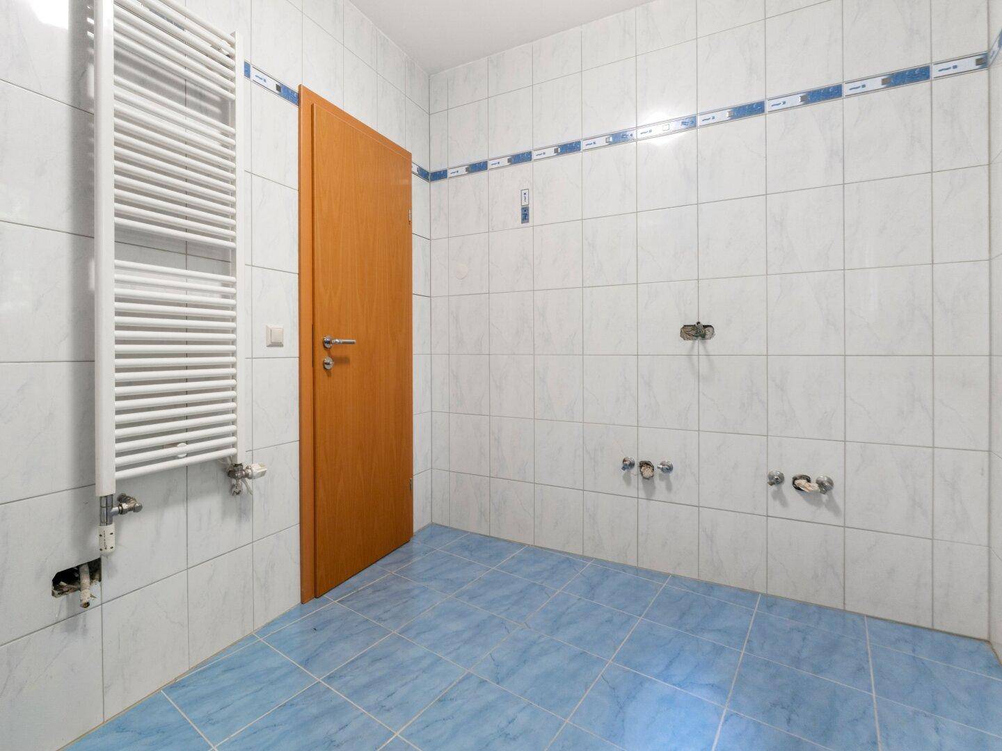Badezimmer mit Fliesenboden und Wandheizkörper, bereit für die Installation von Dusche und Waschbecken.