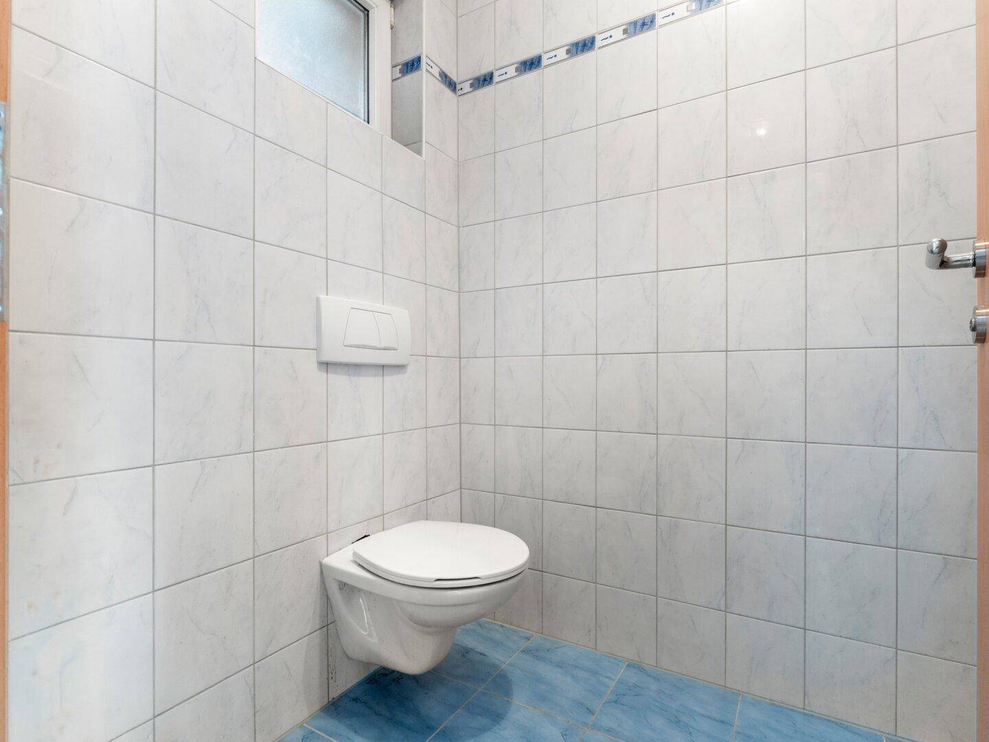 Separates WC mit Wandtoilette und Fenster, komplett gefliest in hellen Farben und sauber.