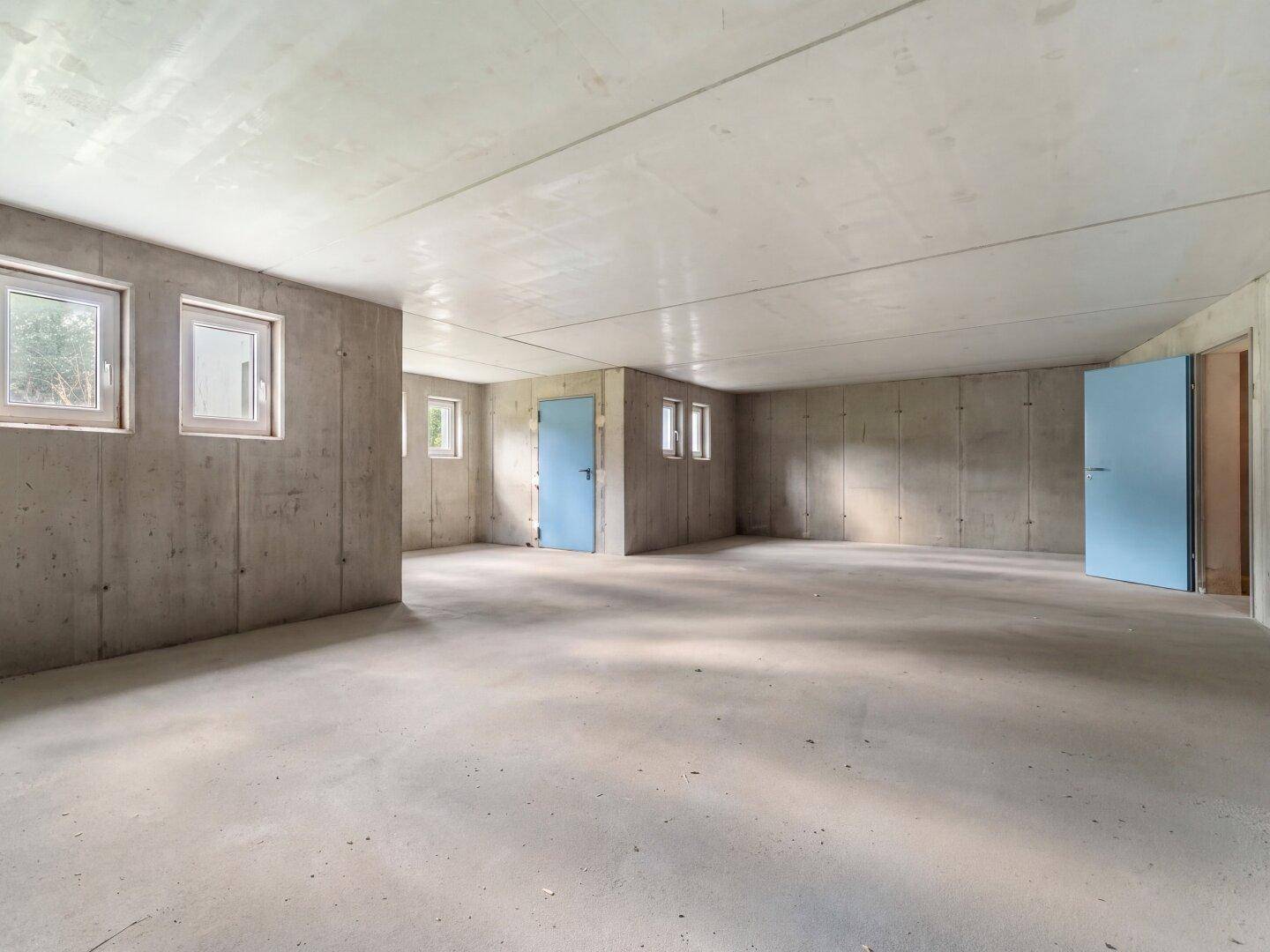 Großer Kellerraum mit Betonboden und mehreren Fenstern, bietet viel Potenzial für Ausbau.