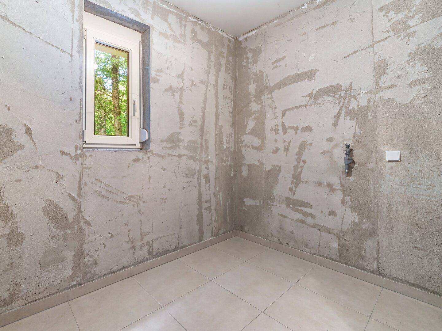 Unfertiger Hauswirtschaftsraum im Keller mit Fenster und Fliesenboden, bereit für den Ausbau.
