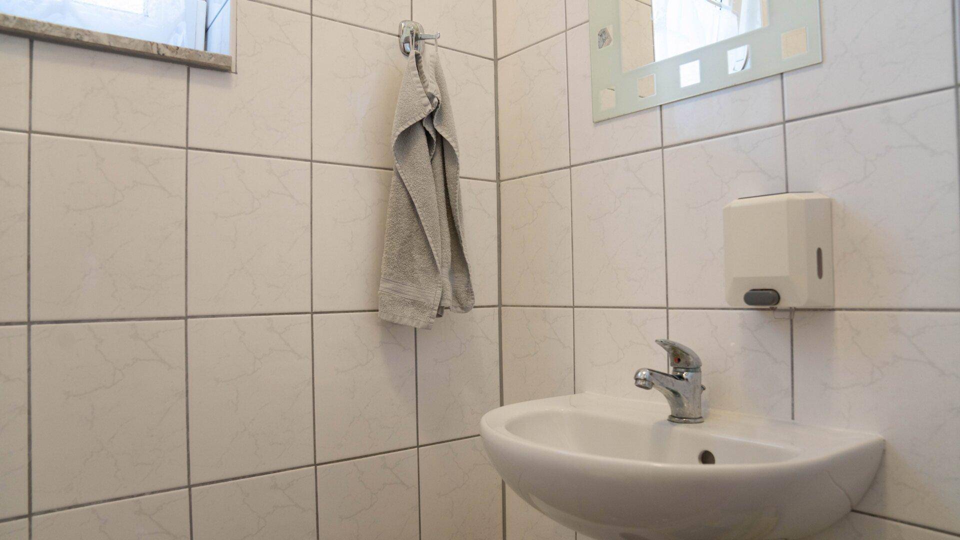 Kleines Waschbecken mit Armatur in einem einfach gefliesten Gäste-WC.