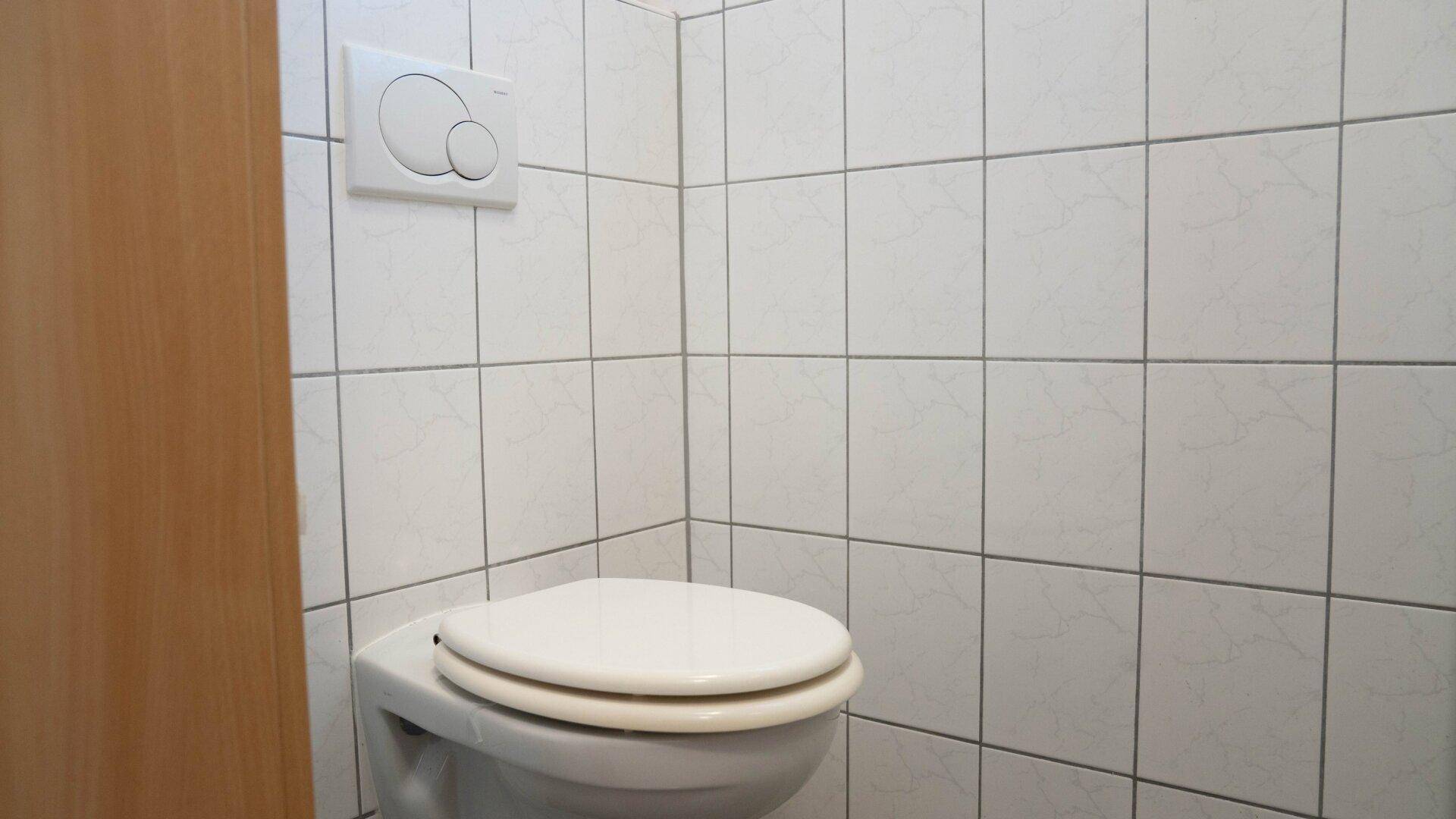 Toilette in einem schlicht gefliesten Raum, passend zu einem Gäste-WC.
