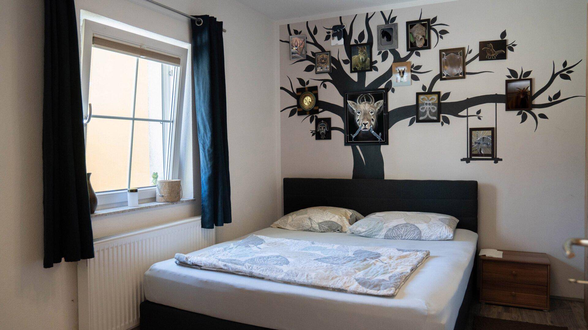 Schlafzimmer mit Doppelbett und einer kreativen Wandgestaltung in Form eines Baumes mit Bilderrahmen.
