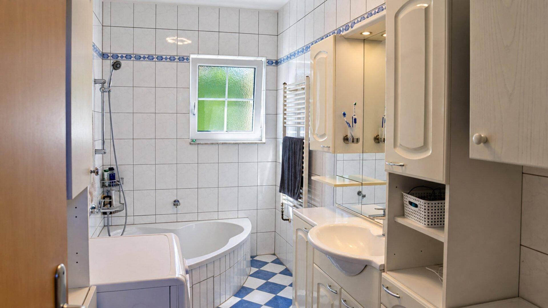 Badezimmer mit weißen Fliesen, blauen Akzenten, Eckbadewanne mit Dusche und Waschbeckenunterschrank.