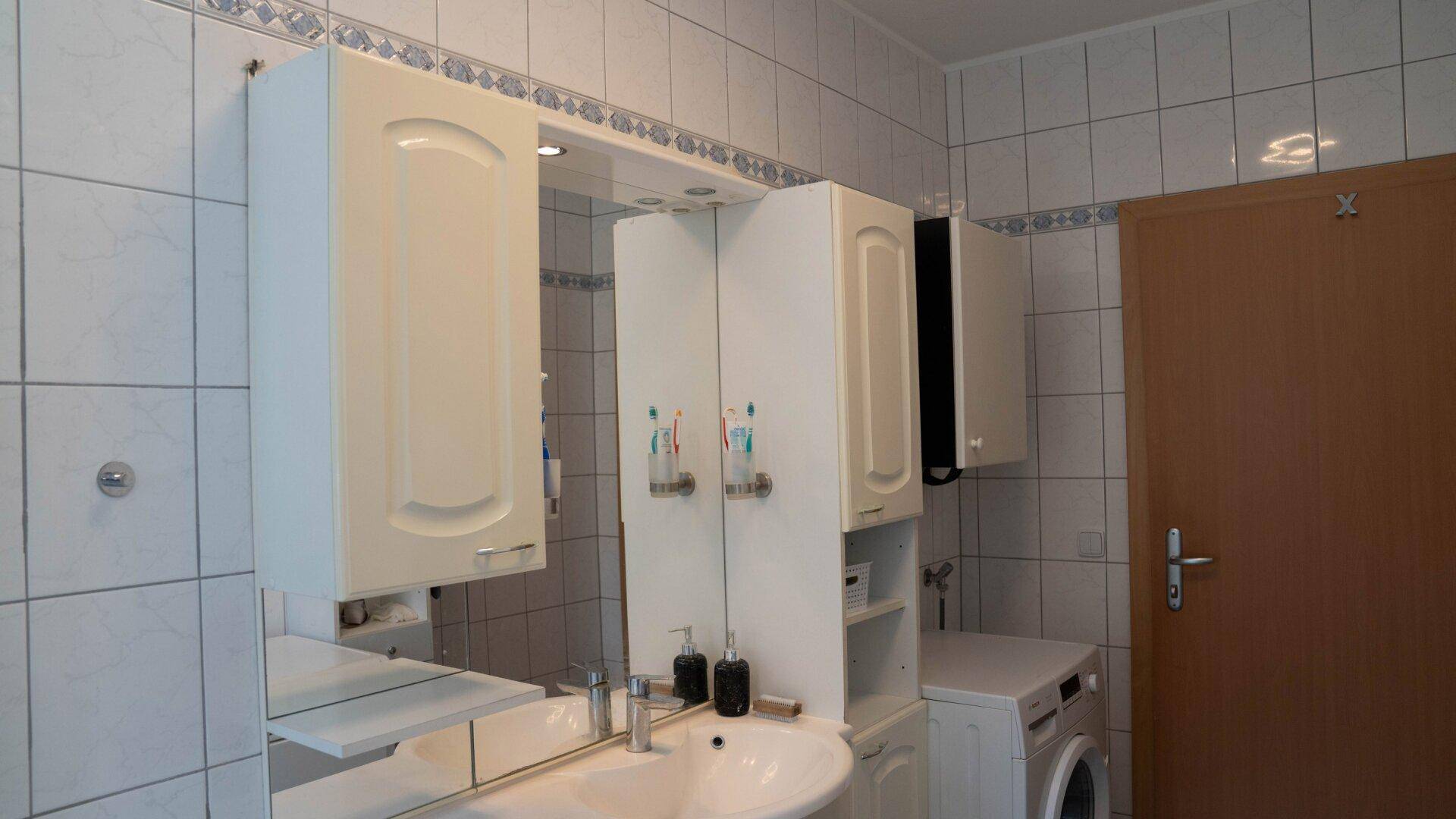 Waschbeckenbereich mit Spiegelschrank und weiteren Hängeschränken im Badezimmer.