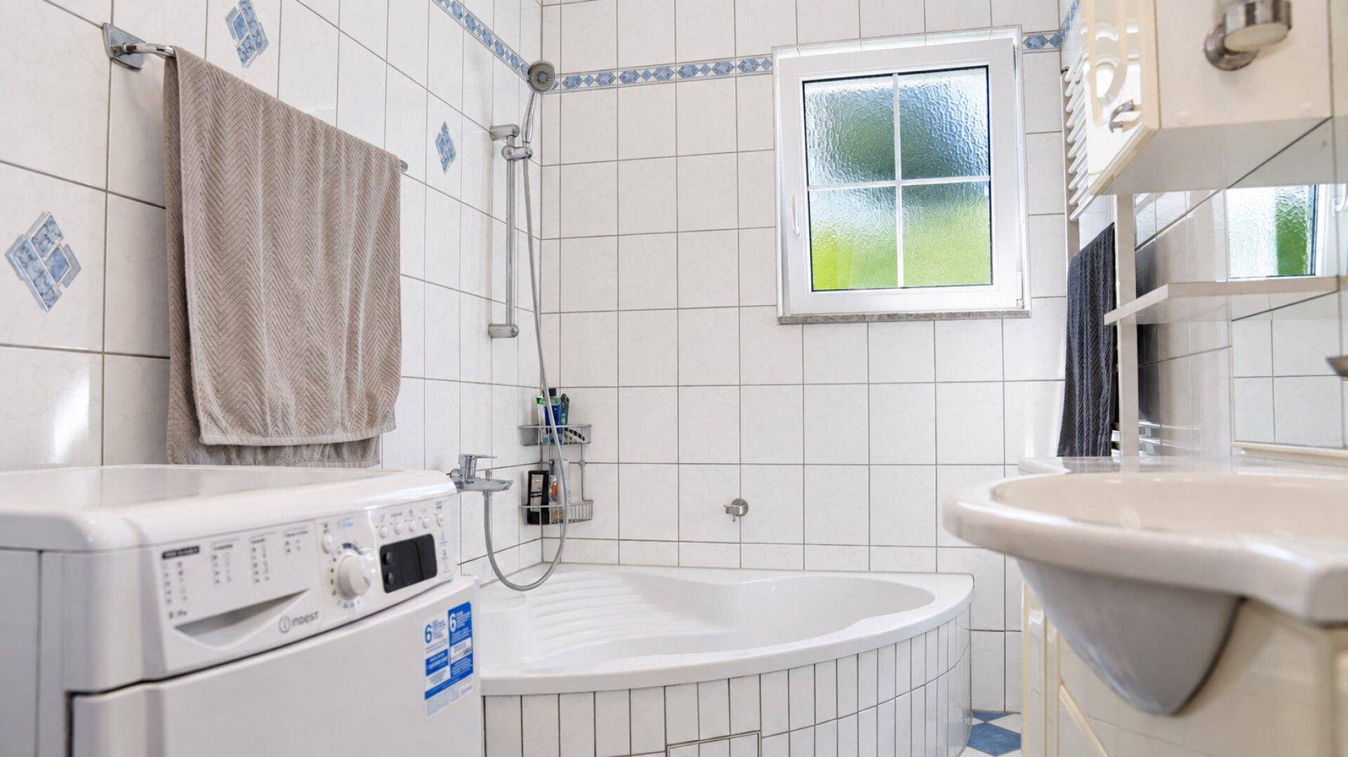 Weitere Perspektive der Eckbadewanne mit Duscharmatur und der Waschmaschine im Badezimmer.