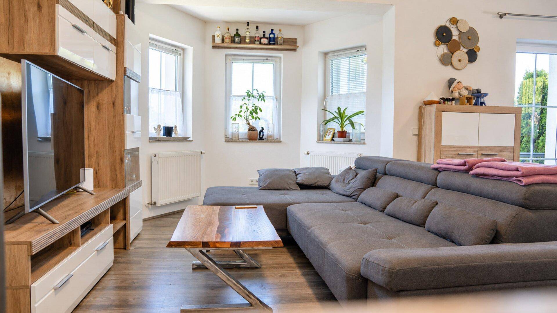 Gemütliches Wohnzimmer mit großem grauen Ecksofa, Holztisch und TV-Möbeln, hell durch Fenster.