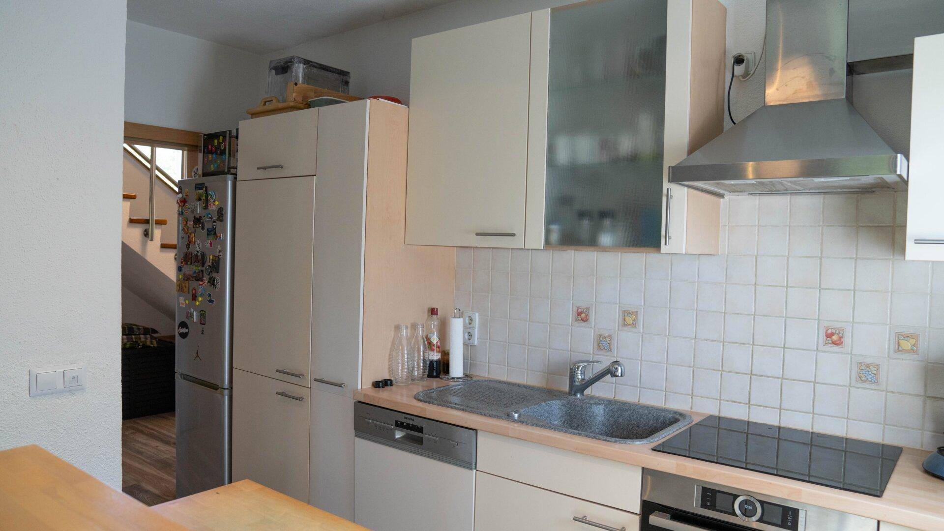 Küchenzeile mit Spüle, Kochfeld, Dunstabzugshaube, Geschirrspüler und Kühlschrank.