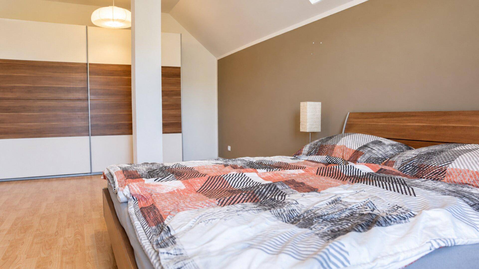 Schlafzimmer mit großem Holzbett, Einbauschränken und Dachschräge.