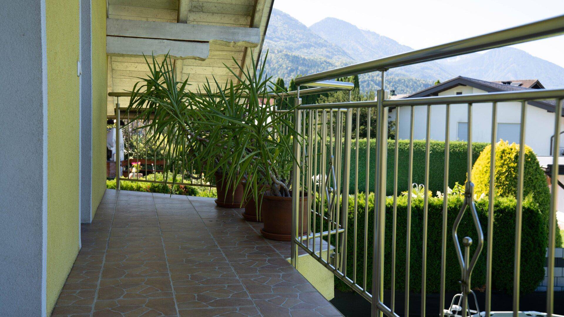 Langer Balkon mit Fliesenboden, Pflanzen und Blick auf die Berge.