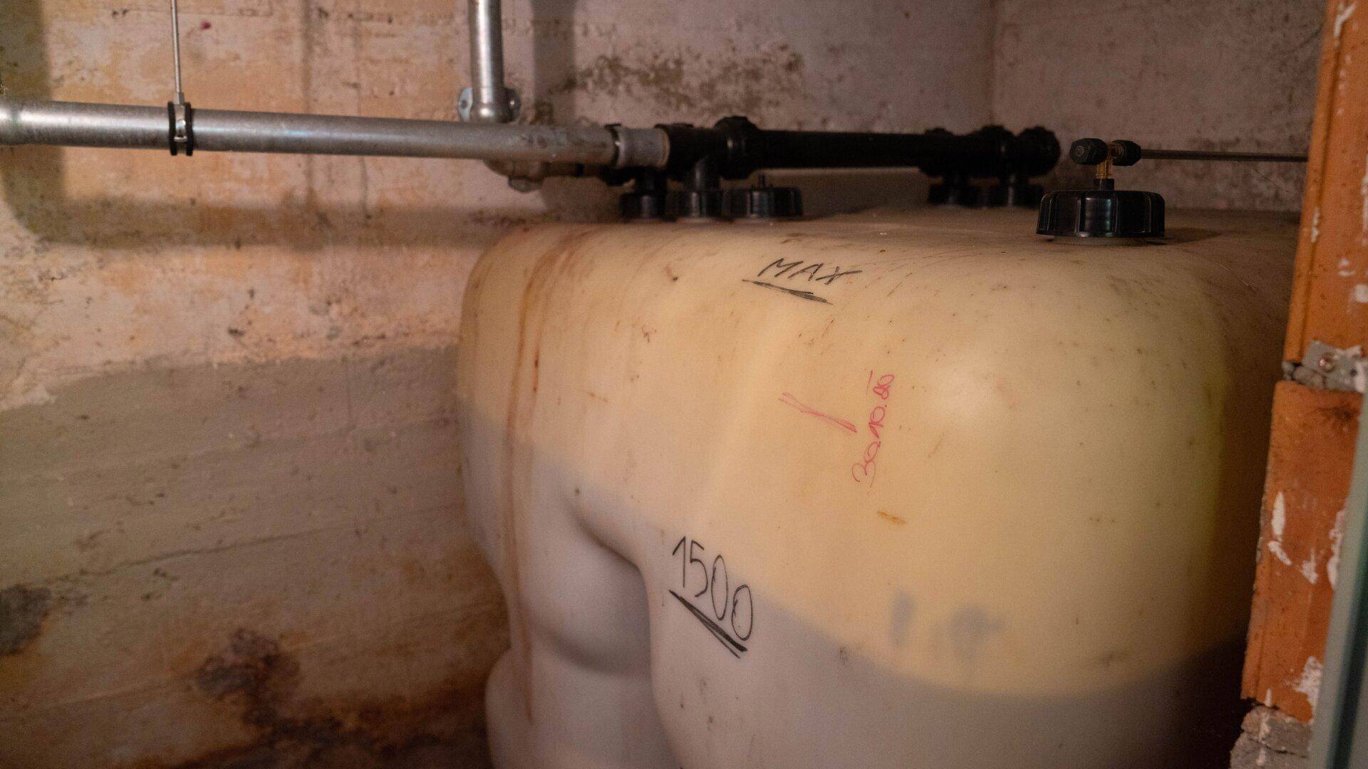 Kellerraum mit großem Wassertank und sichtbaren Rohren an der Wand.
