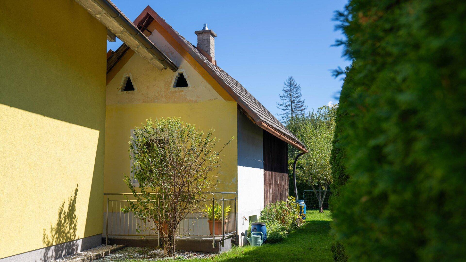 Gelbes Haus mit Satteldach und kleinem Balkon, umgeben von Grünflächen.