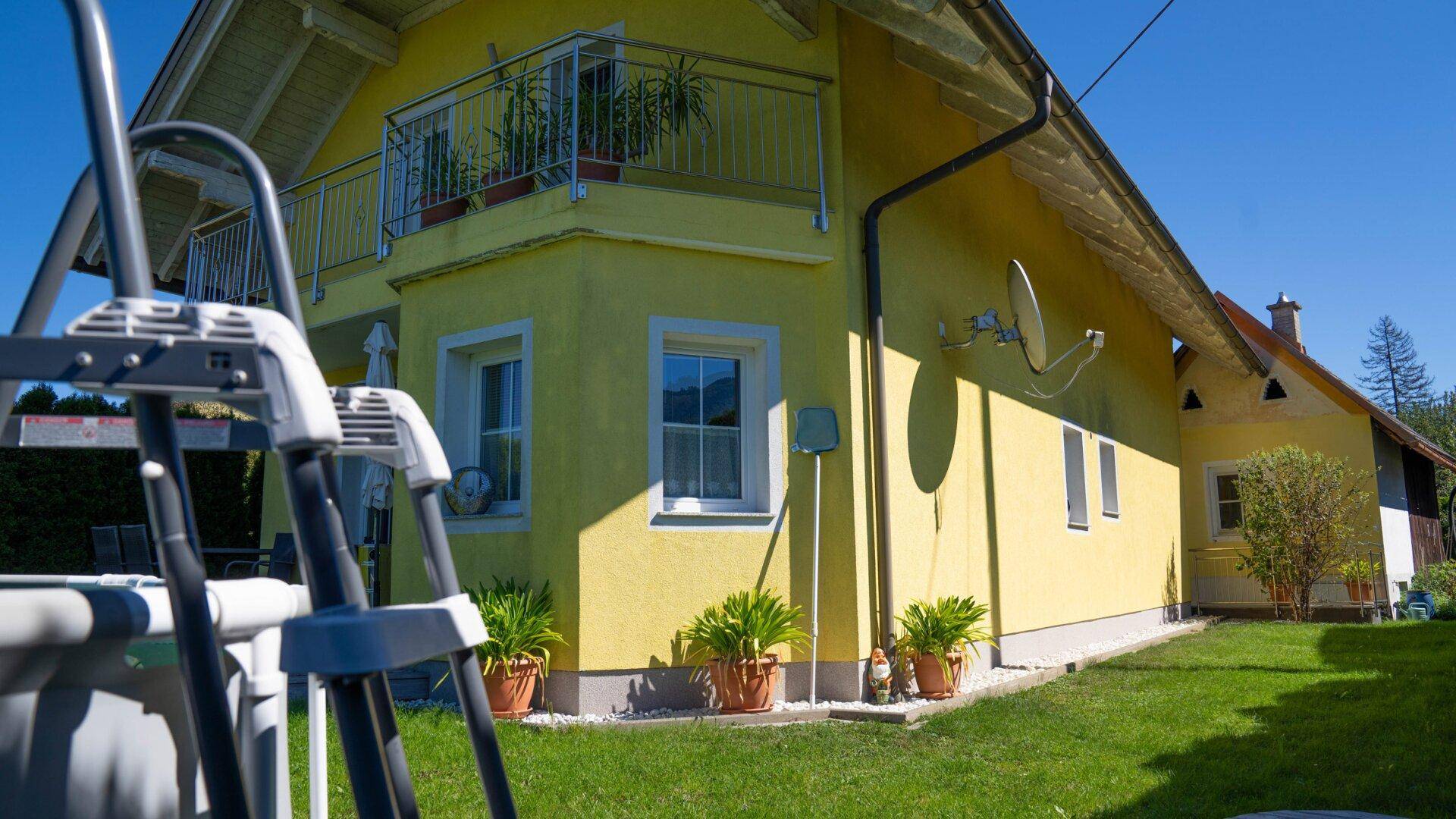 Gelbes Einfamilienhaus mit Balkon und Garten, umgeben von Hecken und Bäumen.