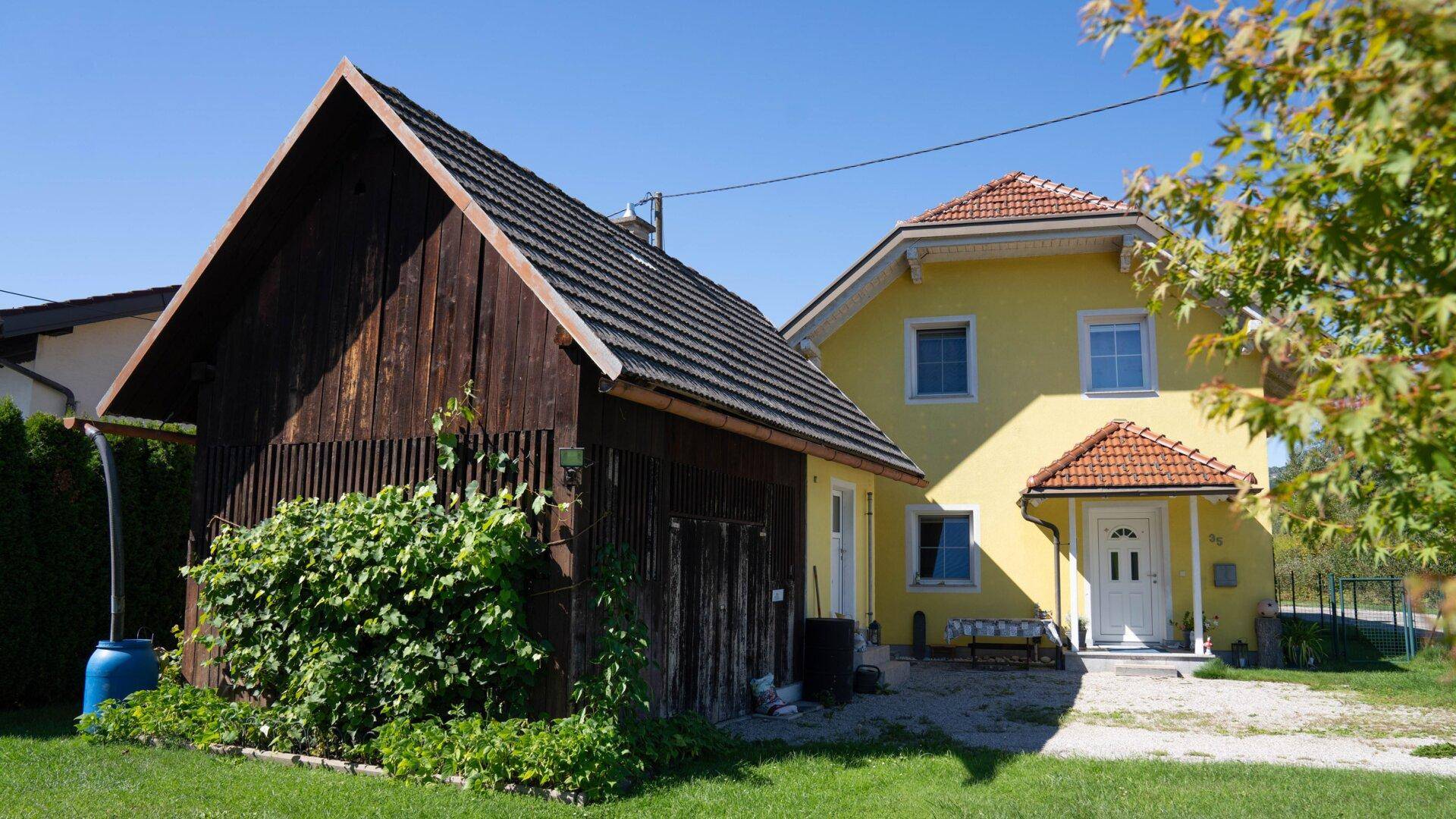 Vorderansicht des gelben Hauses mit Eingangsbereich und dem rustikalen Holzschuppen im Vorgarten.
