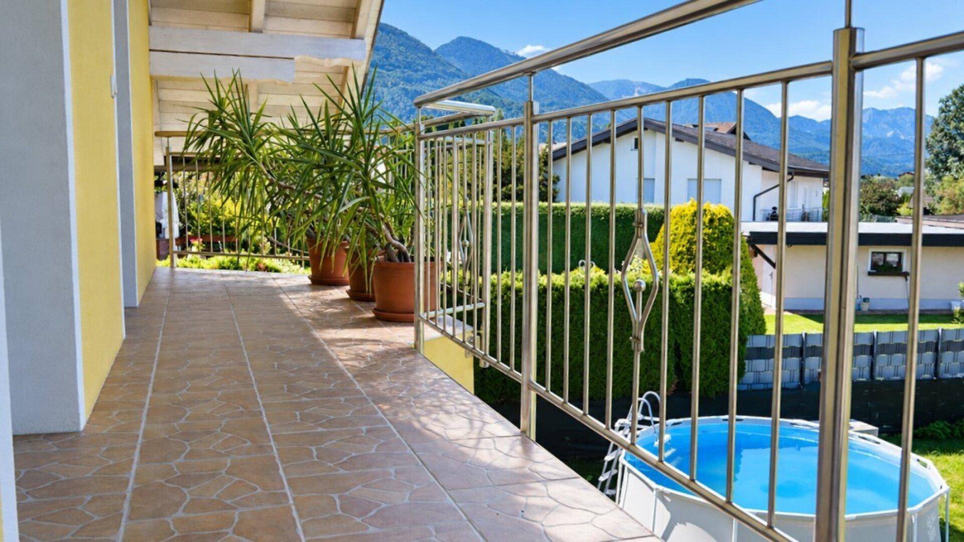 Balkon mit Fliesenboden, Pflanzen und weitem Blick auf Berge und Pool.