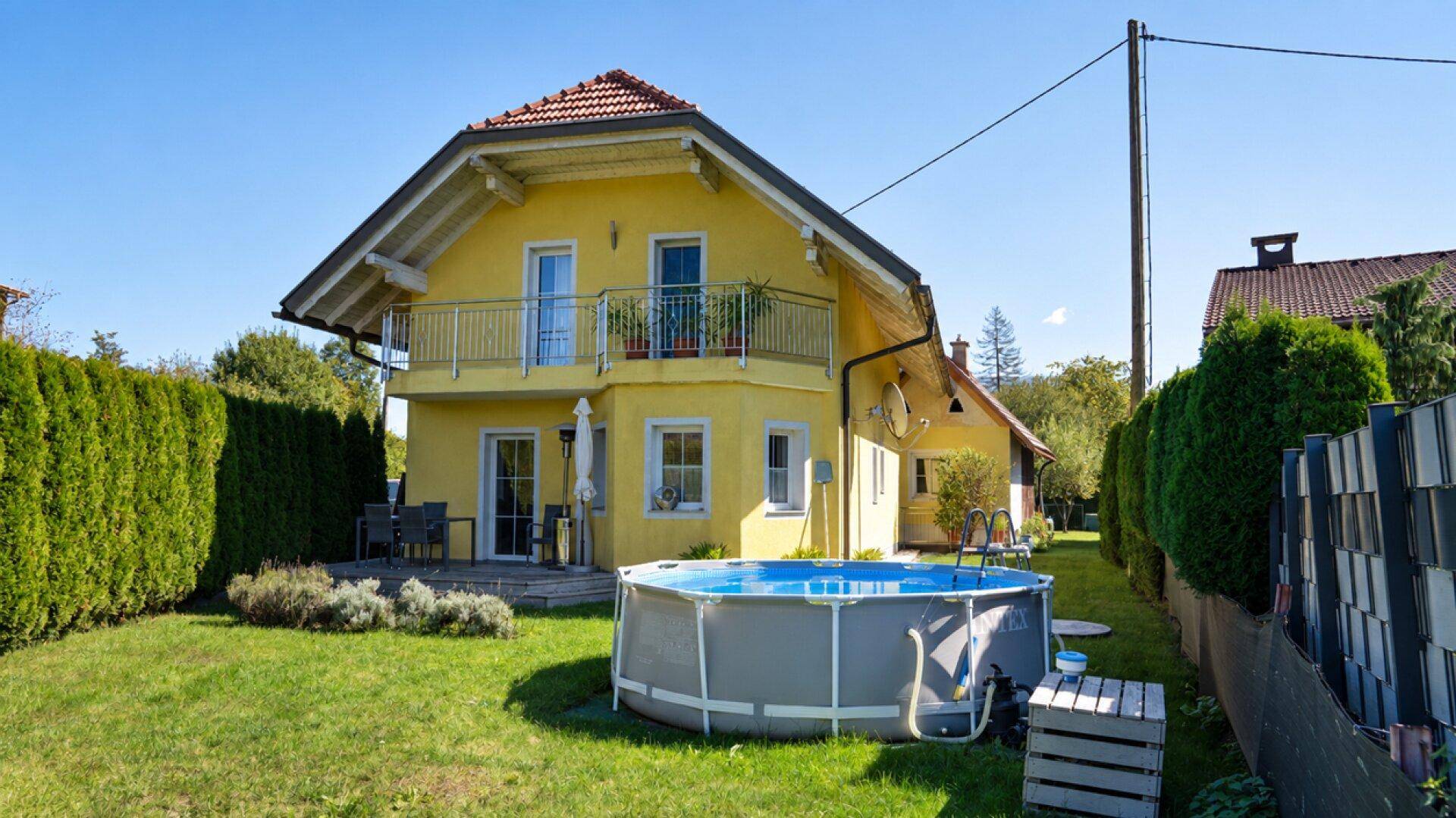 Gelbes Haus mit Garten, Aufstellpool und Terrasse, umgeben von hohen Hecken.