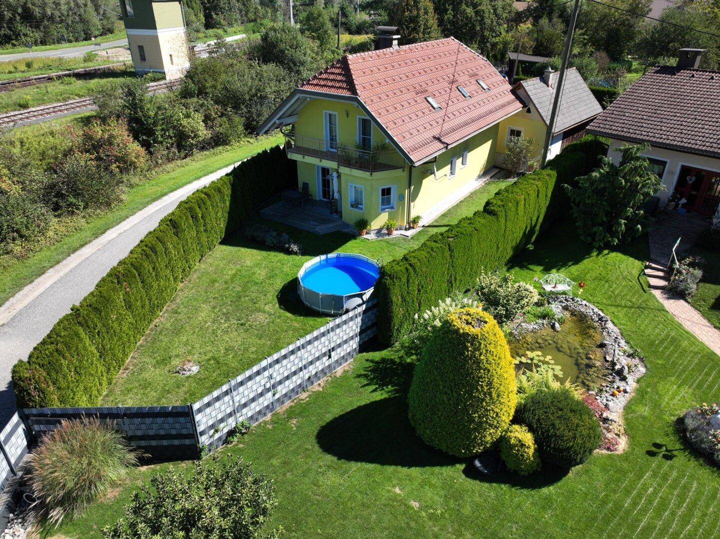 Gartenbereich der Immobilie mit einem kleinen Aufstellpool, einem Teich und einer gepflegten Hecke.