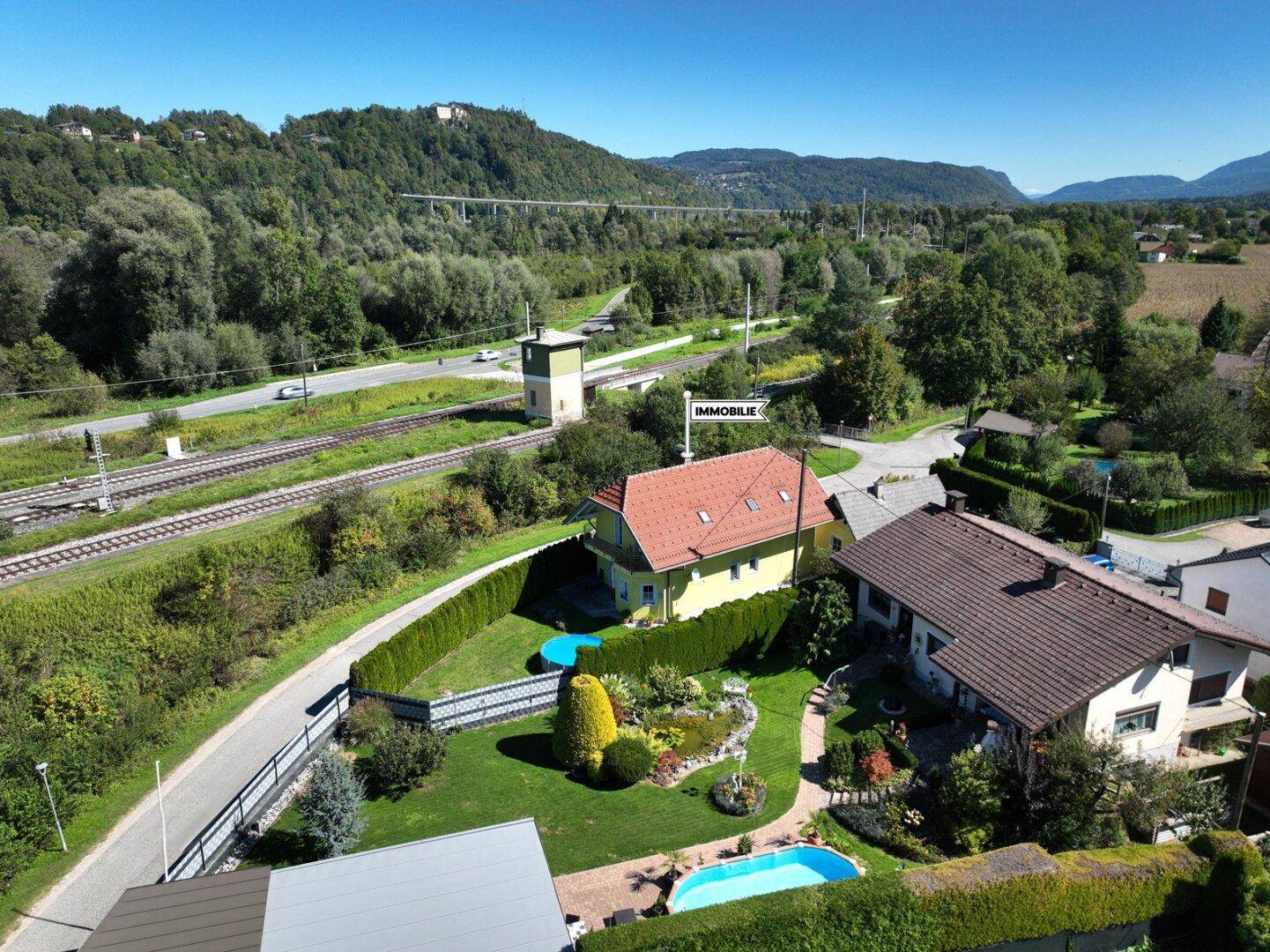 Luftaufnahme des Hauses mit Garten, angrenzenden Bahngleisen und einer Brücke im Hintergrund.