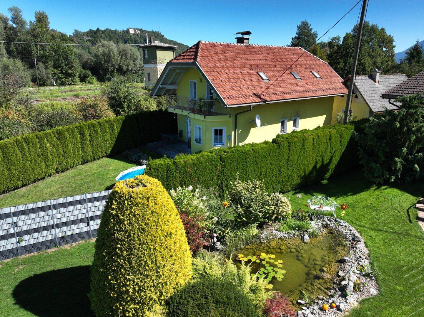 Luftaufnahme des Hauses mit Garten, Teich und umgebender Landschaft.
