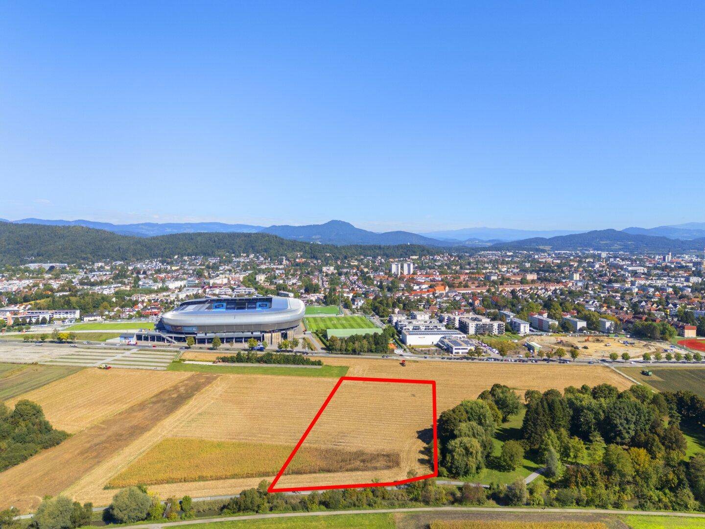 Übersichtsaufnahme eines umrandeten Grundstücks in ländlicher Umgebung mit Stadtpanorama und Stadion.