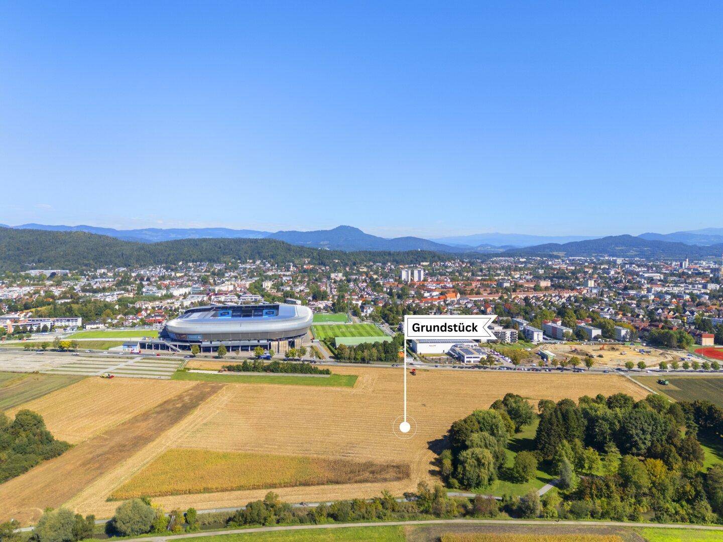 Panoramablick aus der Vogelperspektive auf ein Grundstück nahe einem Stadion mit Stadt im Hintergrund.