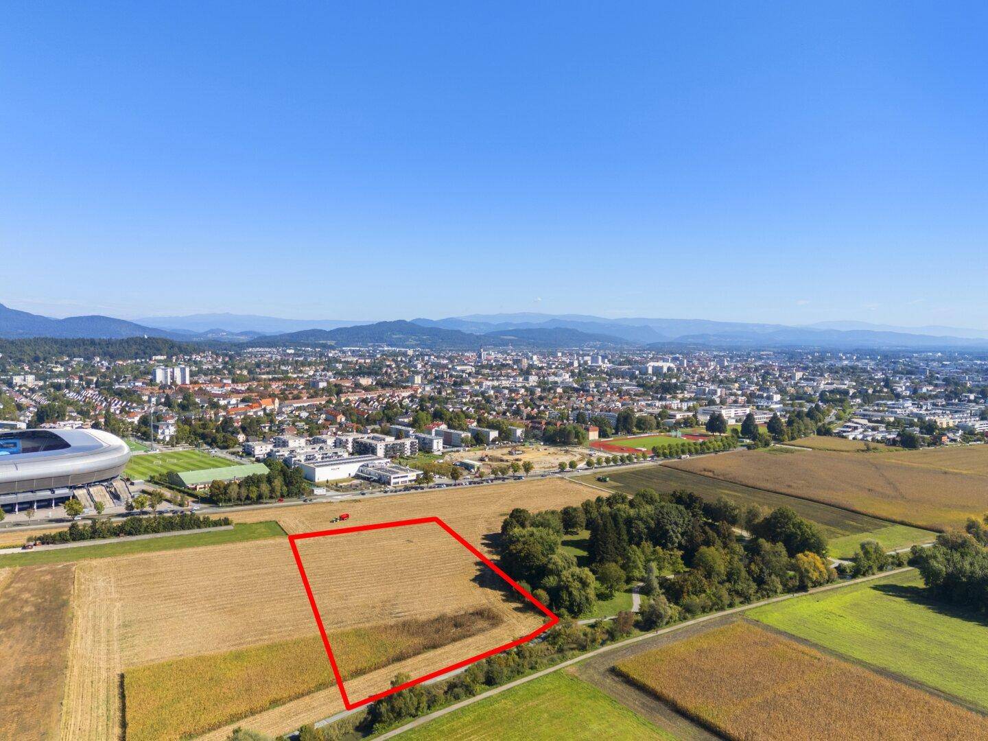 Weitläufige Luftaufnahme eines markierten Grundstücks mit Feldern, Wald und städtischer Kulisse im Hintergrund.