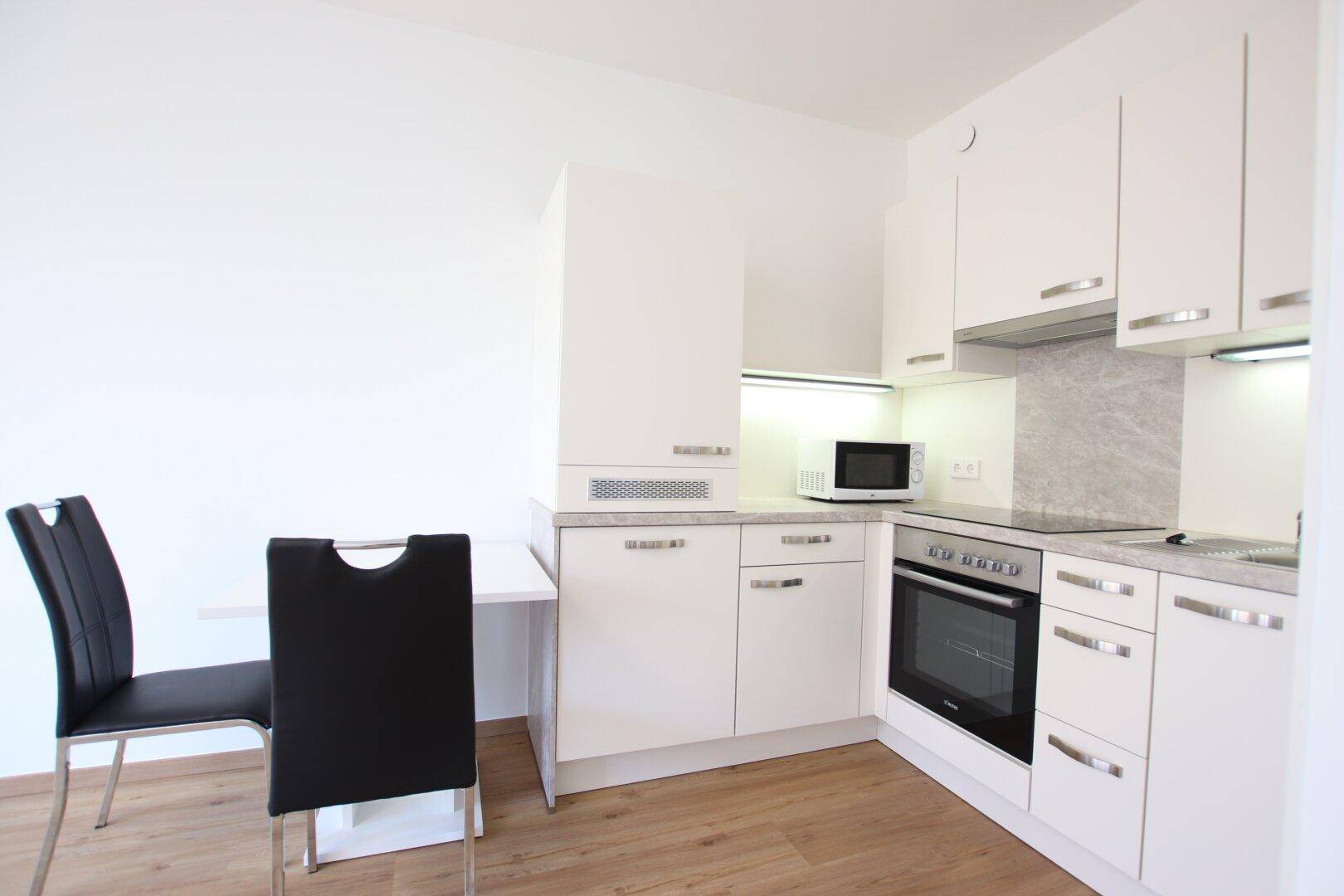 Moderne Küchenzeile mit weißen Schränken, integriertem Backofen und Mikrowelle.