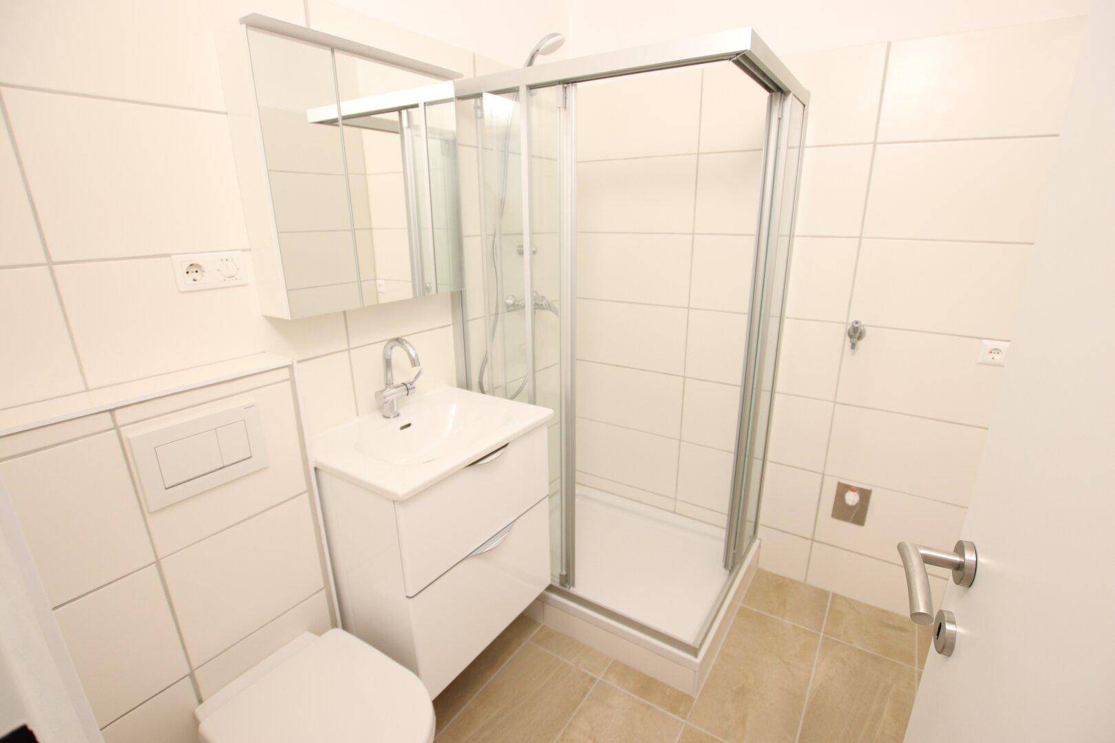 Modernes Badezimmer mit Duschkabine, WC, Waschbecken und weißen Fliesen.
