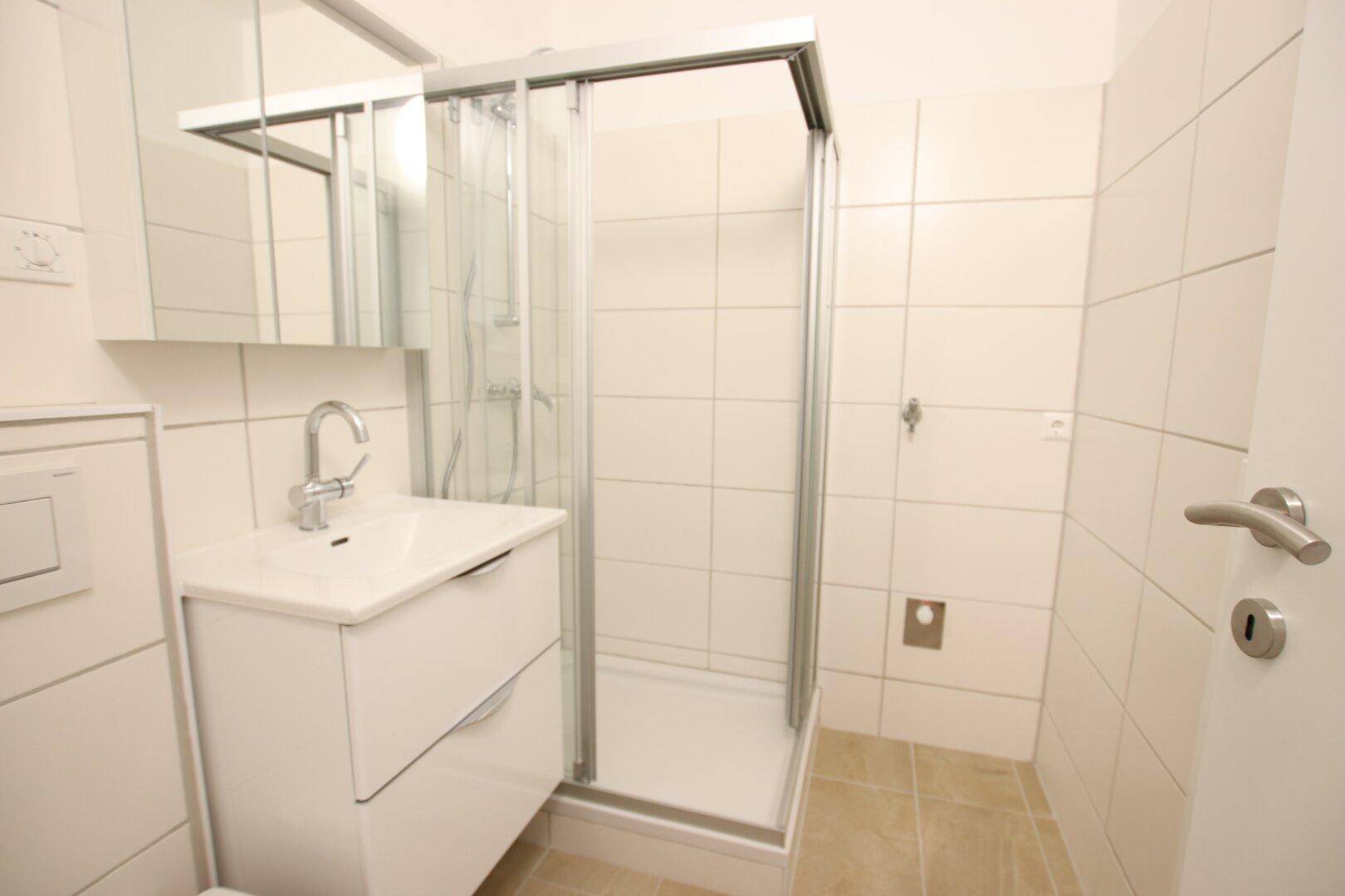 Helles Badezimmer mit Duschkabine, Waschbeckenunterschrank und weißen Wandfliesen.
