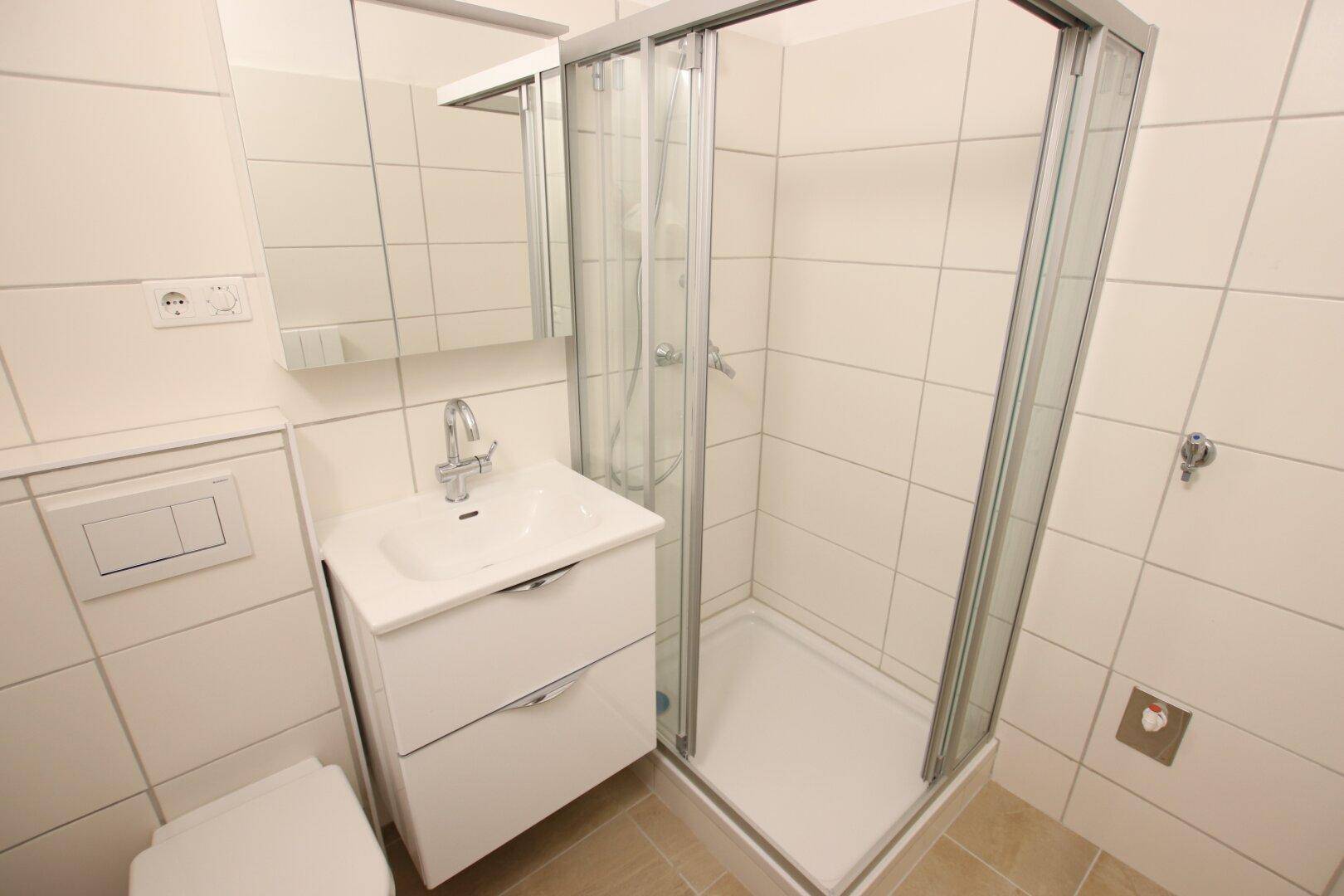 Funktionales Badezimmer mit Duschkabine, WC und Waschbecken, ausgestattet mit weißen Fliesen.