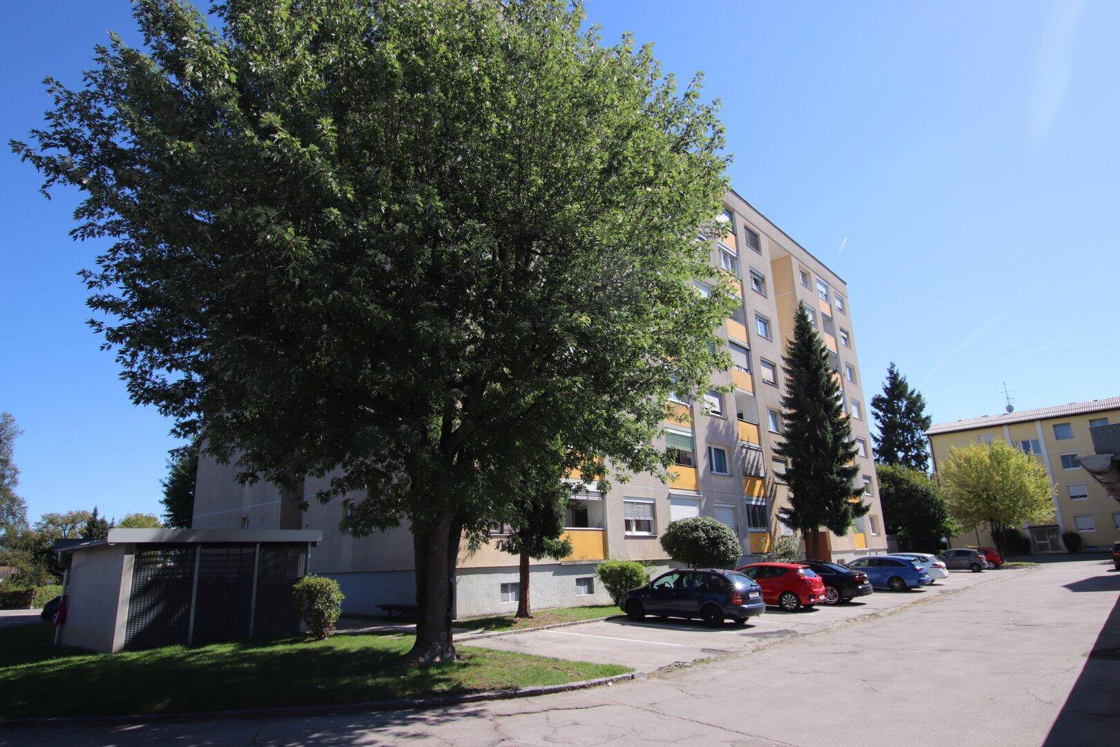 Wohngebäude in grüner Umgebung mit Bäumen und Parkmöglichkeiten für Bewohner.