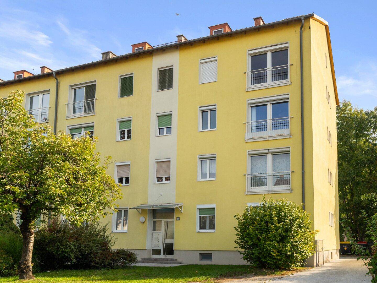 Gelbes Mehrfamilienhaus mit mehreren Balkonen und grüner Umgebung.