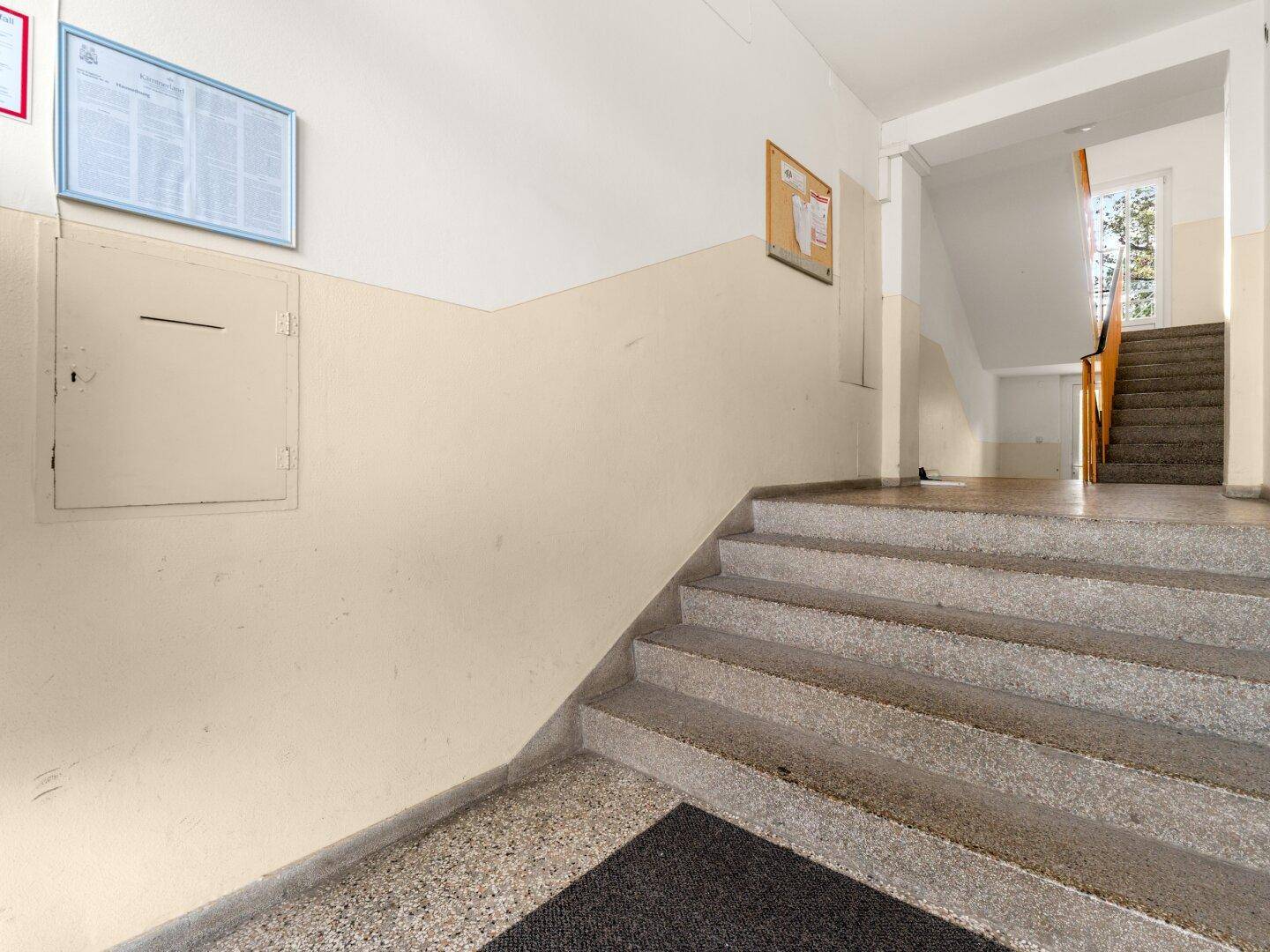 Treppenhaus mit Terrazzoboden und beigefarbenen Wänden in einem Mehrfamilienhaus.