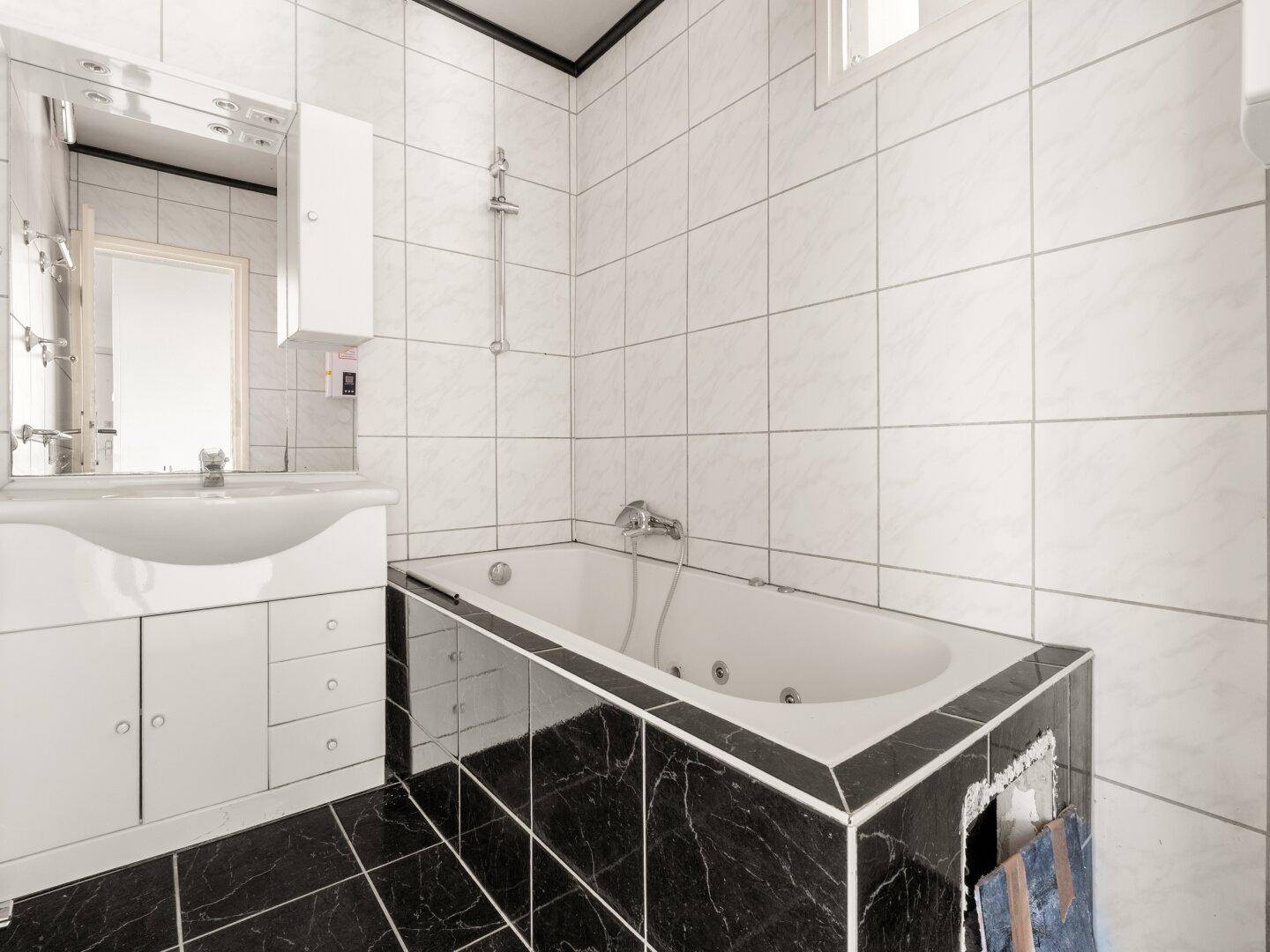 Badezimmer mit gefliesten Wänden, Badewanne mit Duschfunktion und Waschbecken.