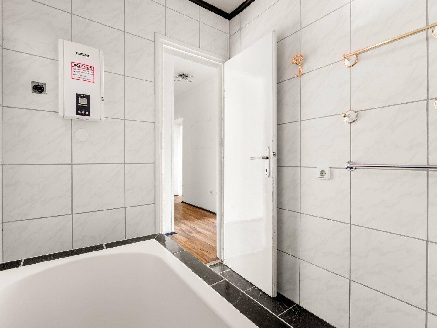 Badezimmer mit Wandfliesen und Blick in den angrenzenden Raum.
