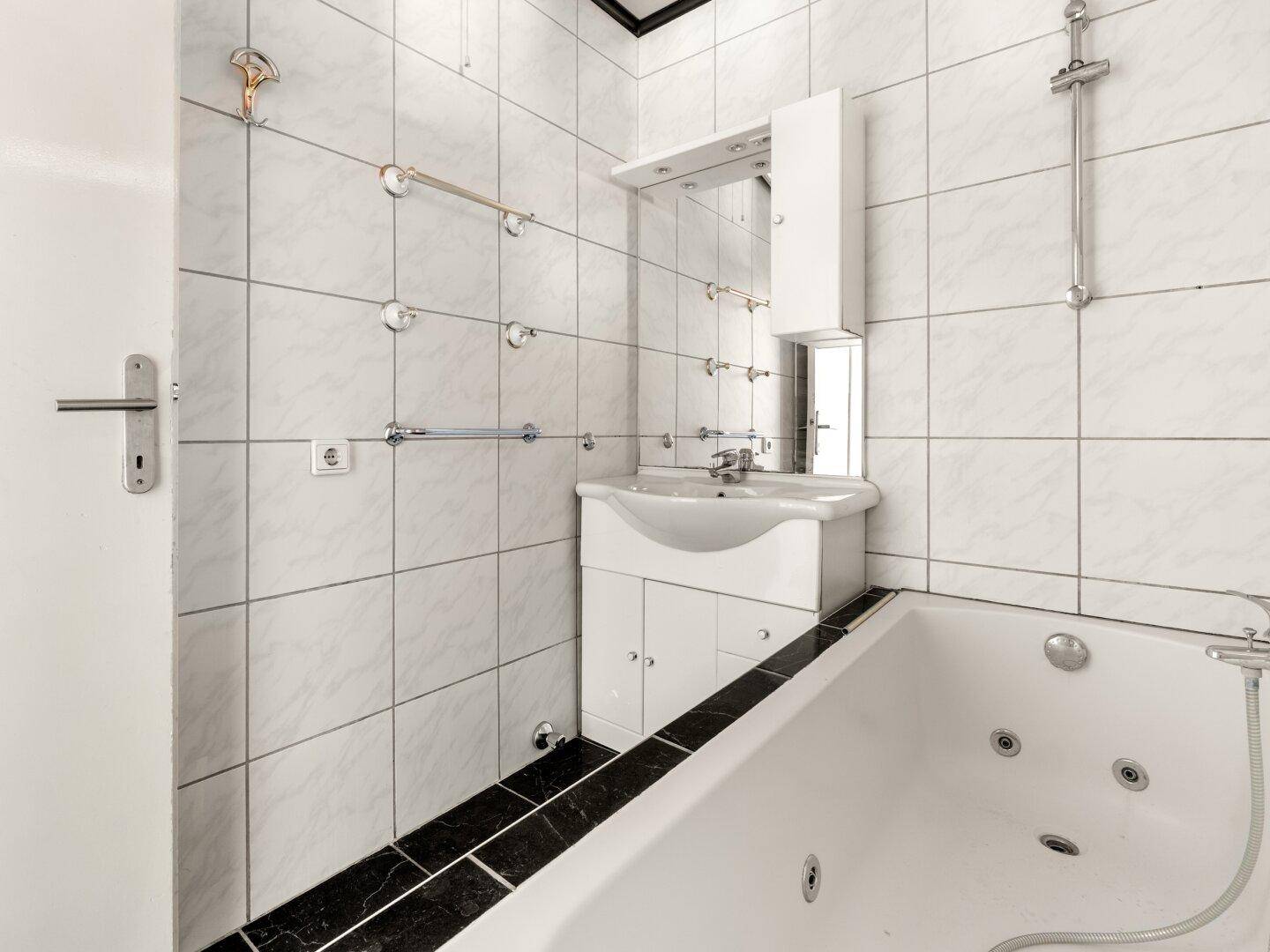 Gefliestes Badezimmer mit Badewanne, Waschbecken und Spiegelschrank.